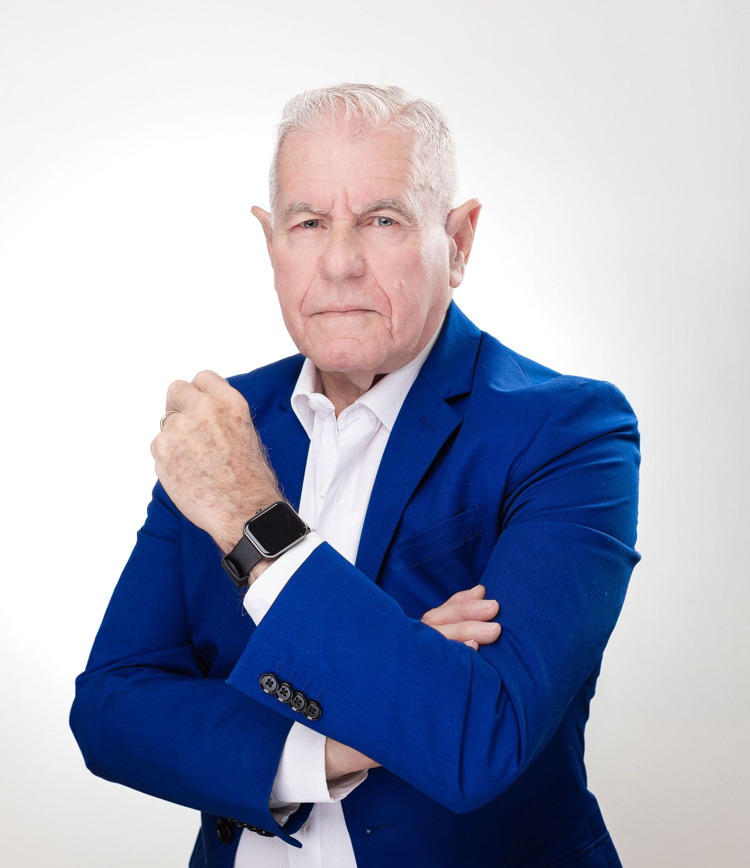 Professional headshot of person in blue blazer and white shirt with smart watch against white background.