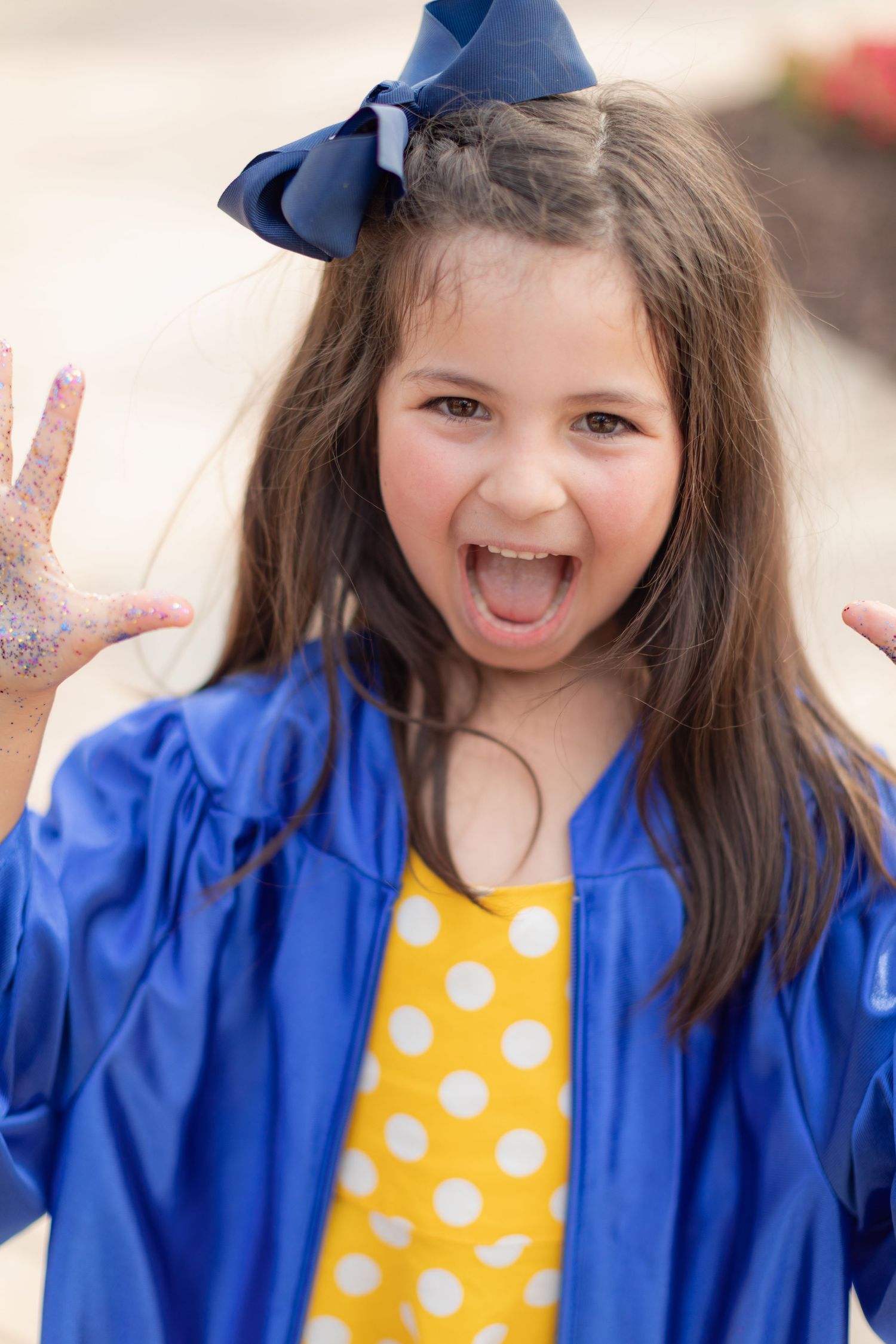 Child in bright blue jacket and yellow polka dot shirt shows excited expression with hands raised.