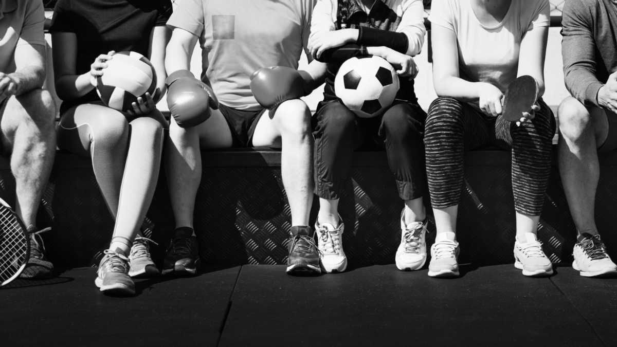 Black and white image showing legs in athletic wear and sneakers with soccer balls held at waist level.