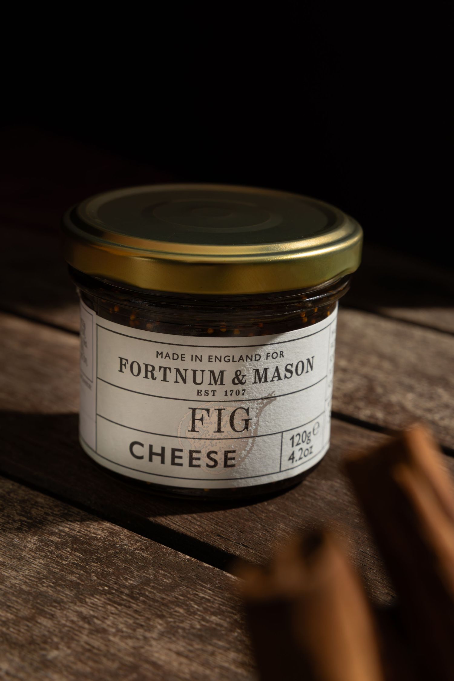 Three vintage Fortnum & Mason branded food jars with gold lids sit on a rustic wooden surface in moody lighting.