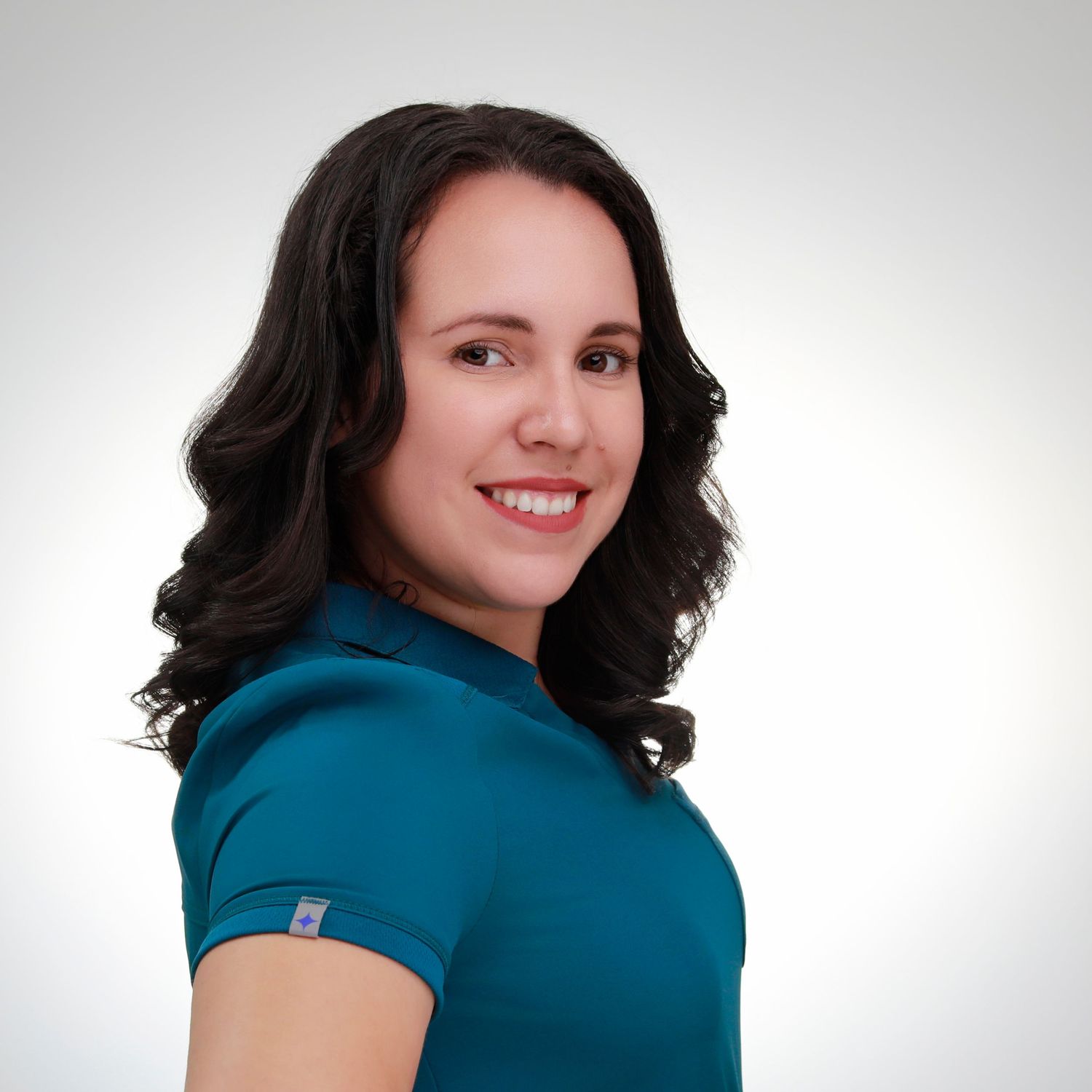 Professional headshot in teal top with wavy dark hair against white background.