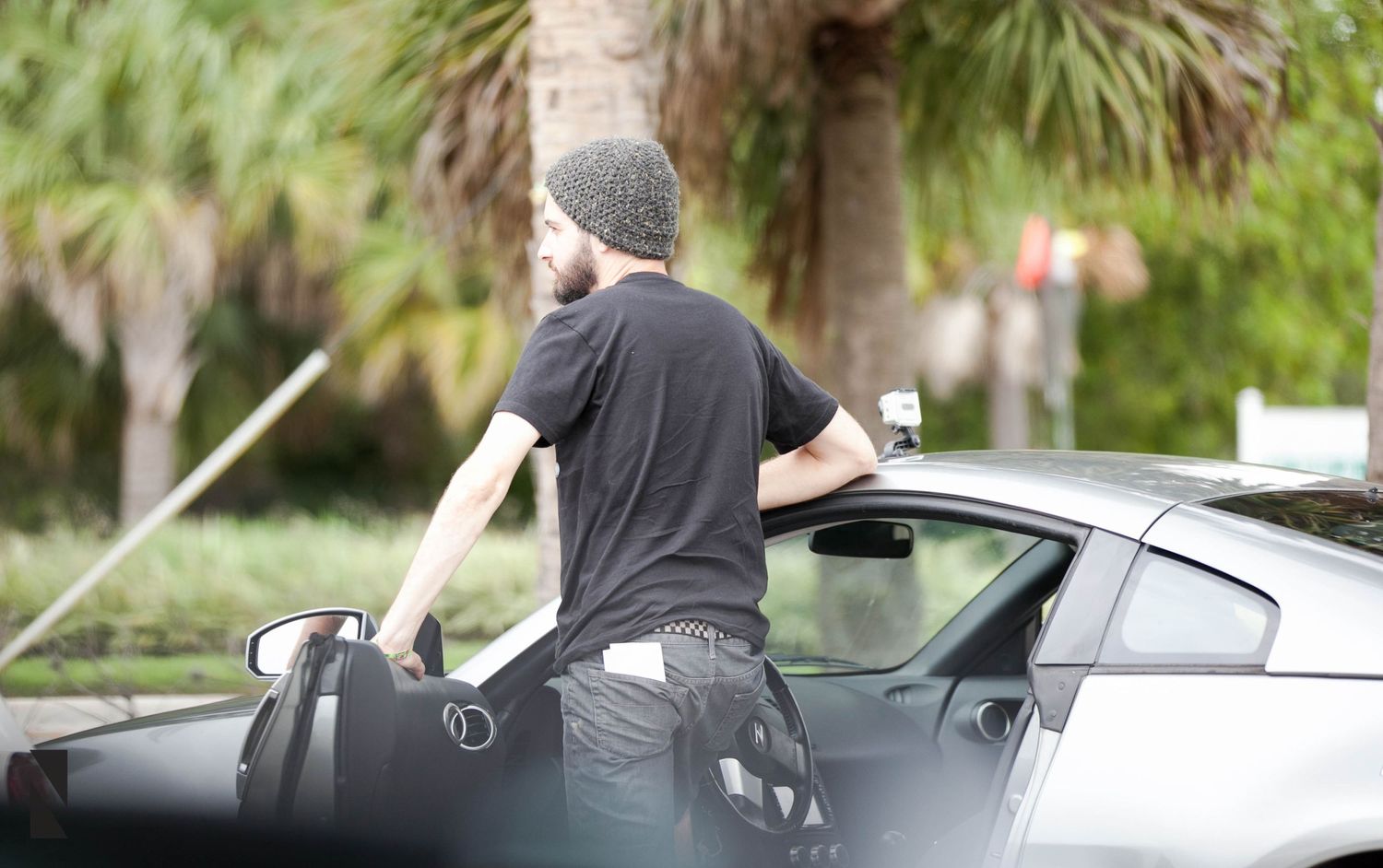 Someone in casual clothing with a beanie hat loads sports equipment into the trunk of a silver car.