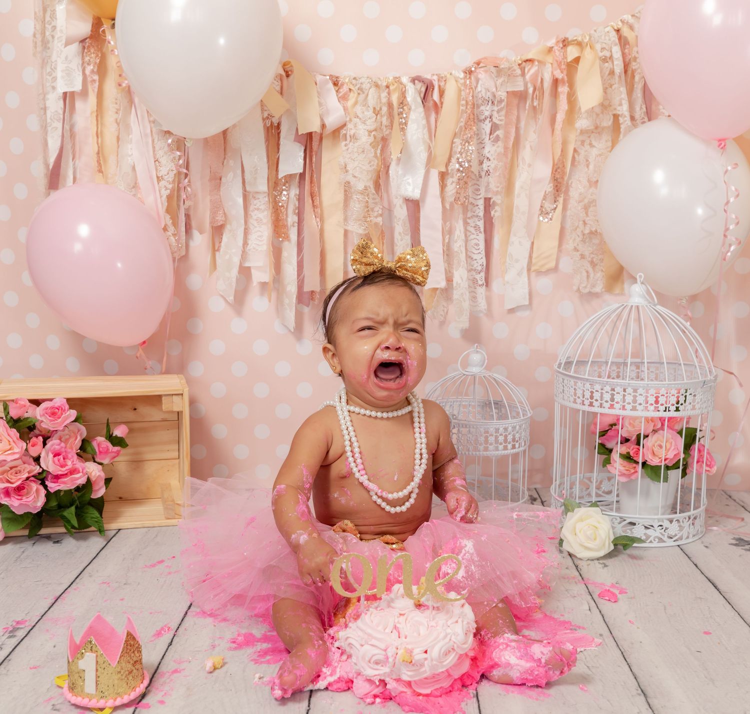 Pink and white cake smash photo setup with tutu, balloons, birdcage and wooden crate decorations.