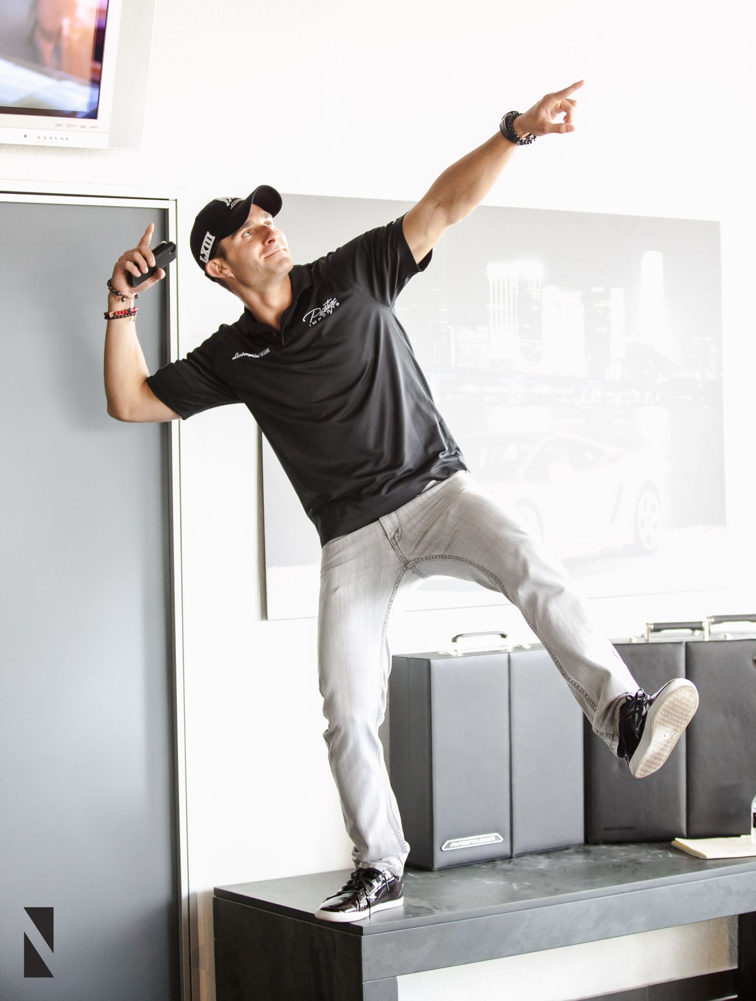 Person in black polo and light pants striking dynamic pose on elevated platform in interior setting.