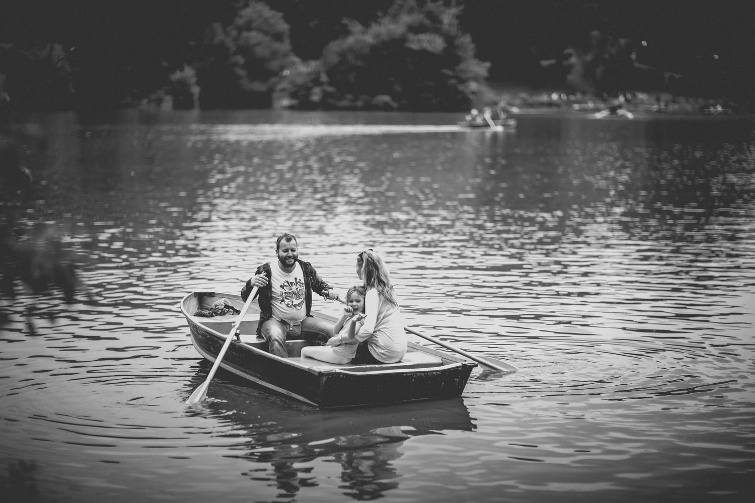 Black and white photo of people rowing a small boat on a tranquil lake.