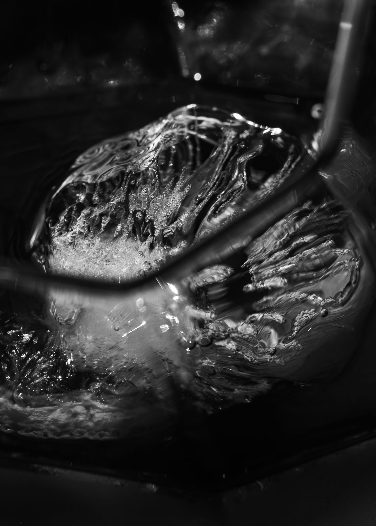 Close-up black and white photograph of a walnut being cracked in dark liquid with dramatic lighting.