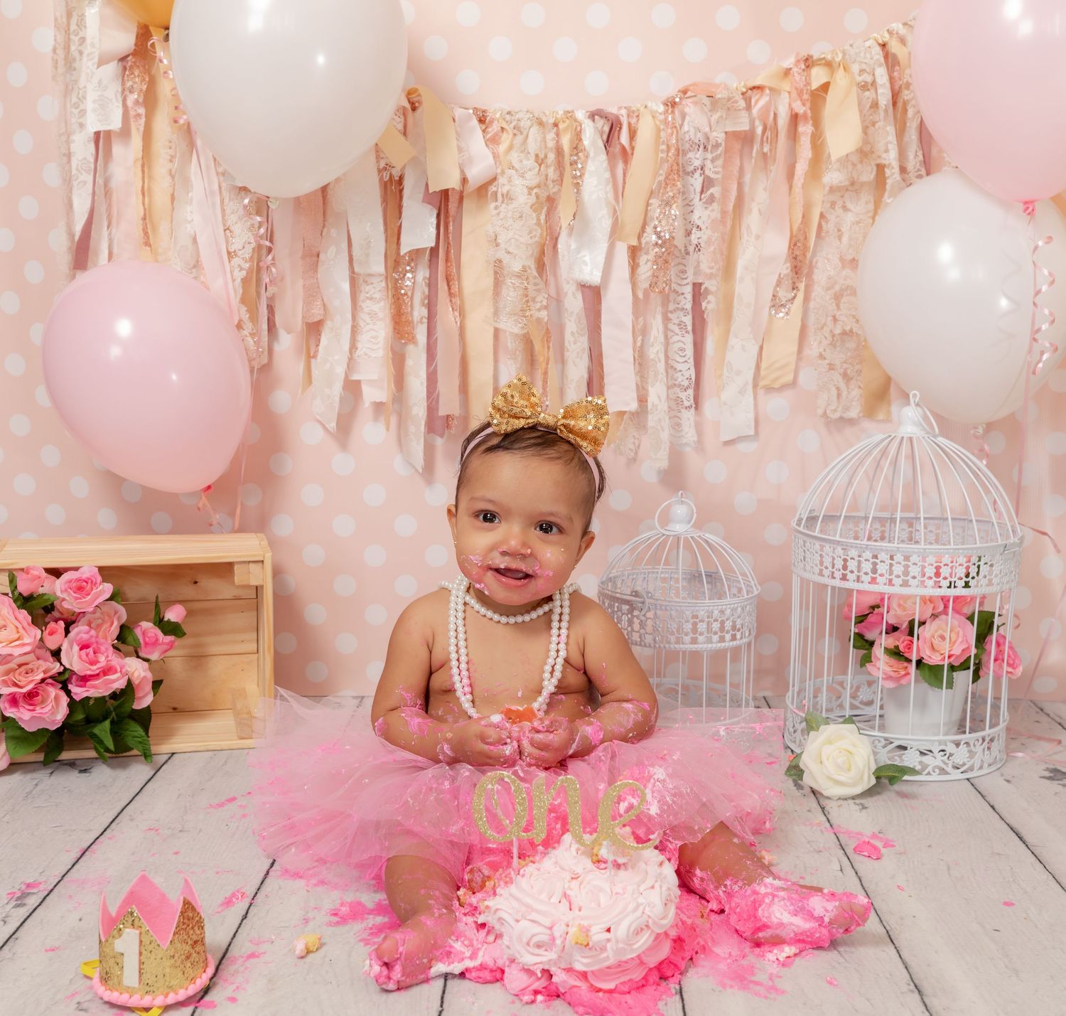 First birthday celebration setup with pink tutu, cake smash, balloons, birdcages and floral decorations against fabric backdrop.