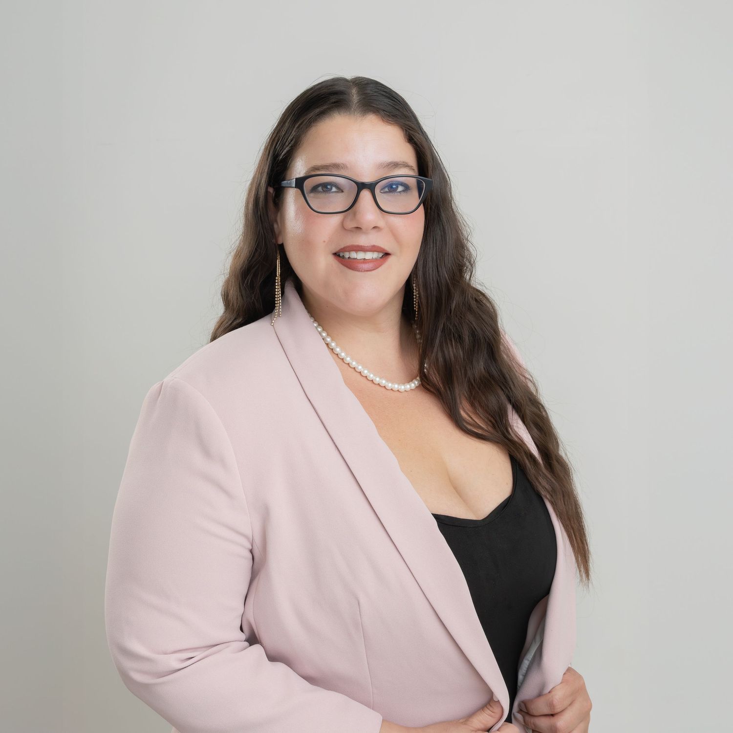 Professional portrait in a soft pink blazer and black top with glasses against a light background.