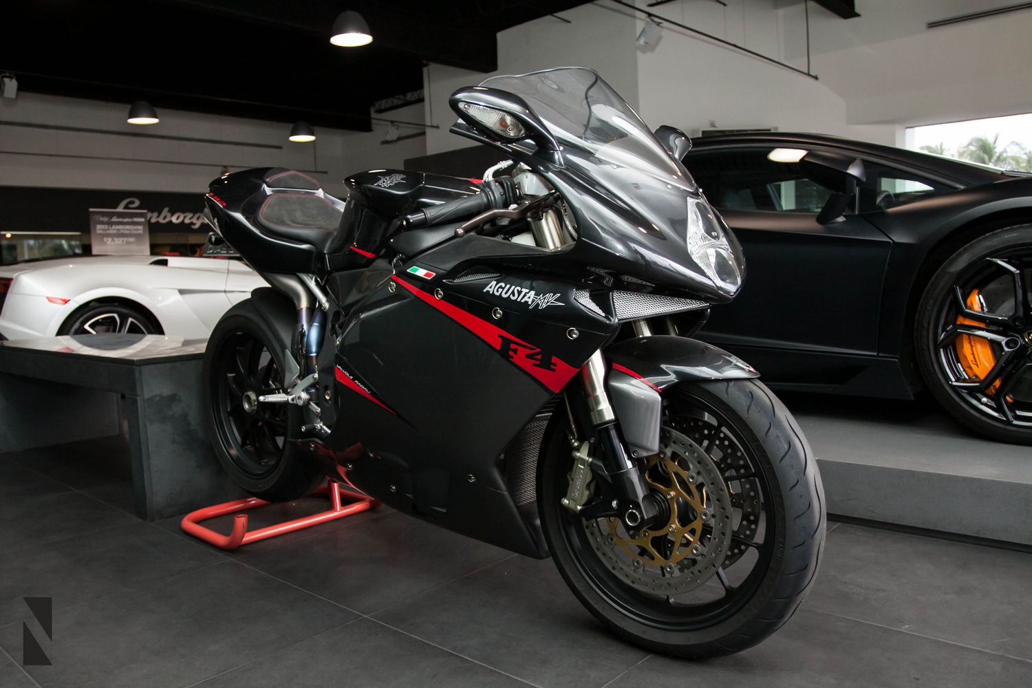 Black and red Ducati superbike parked in a dimly lit garage alongside luxury sports cars.