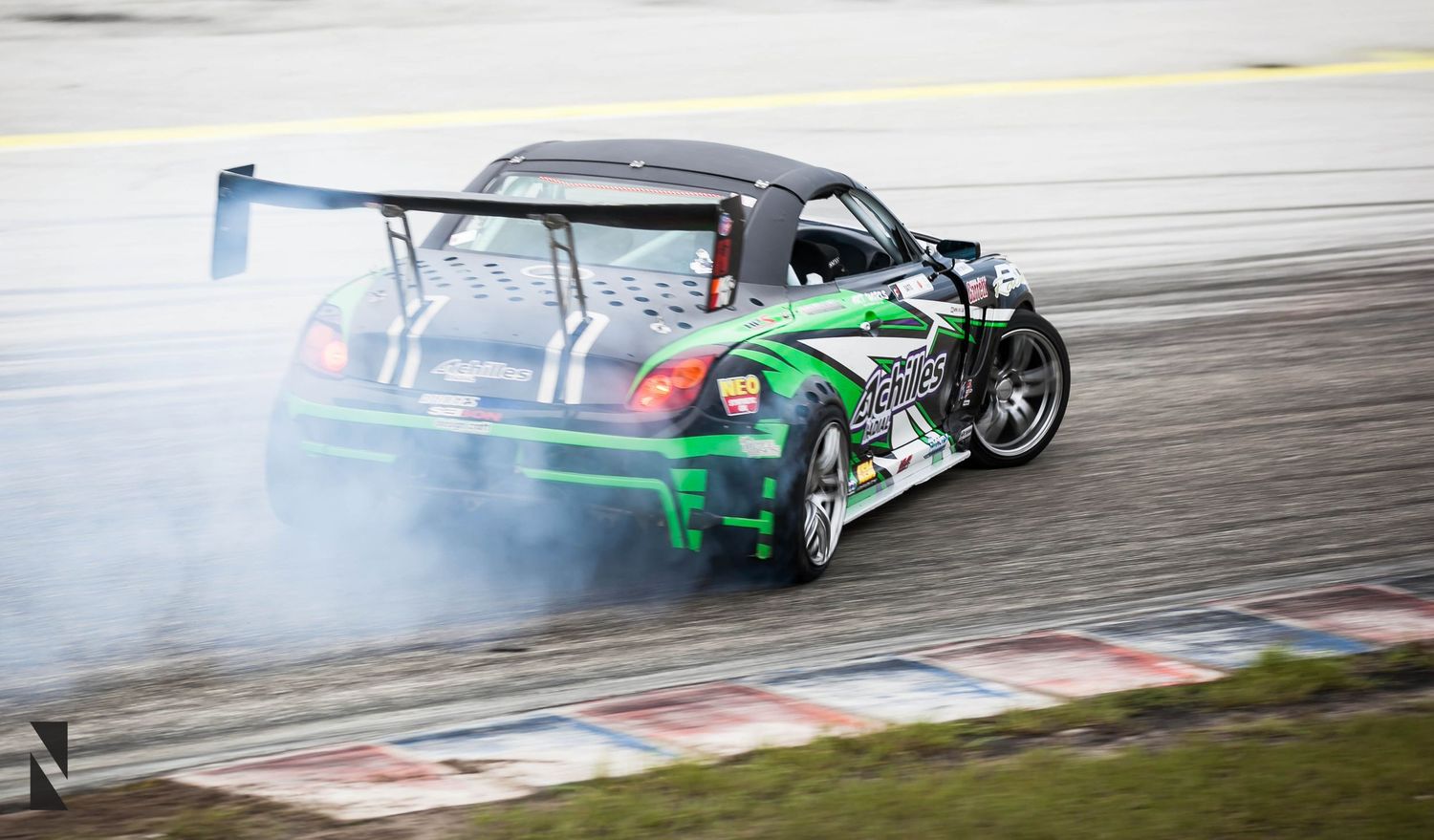 Green drift racing car sliding sideways on track with smoke billowing from tires during competition event.