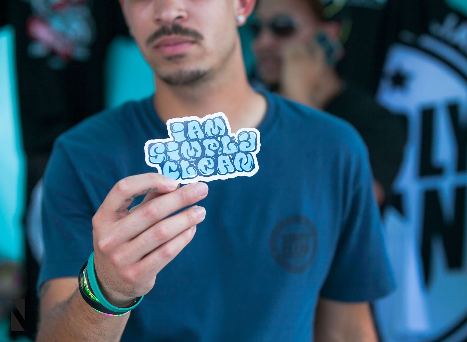 Person in blue shirt holding up a sticker with text design against dark background.