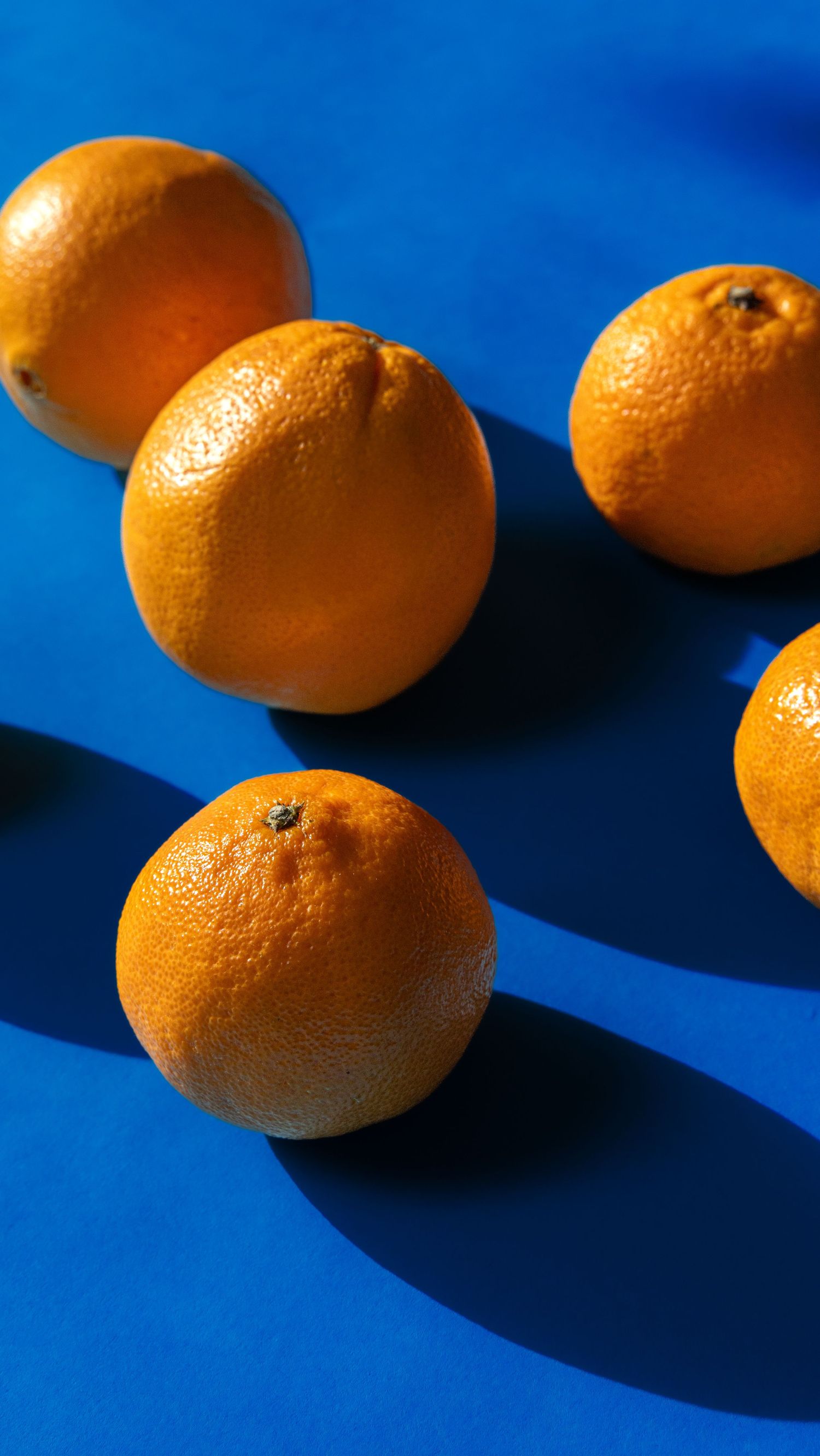 Fresh oranges casting dramatic shadows on vibrant blue background in artistic still life composition.