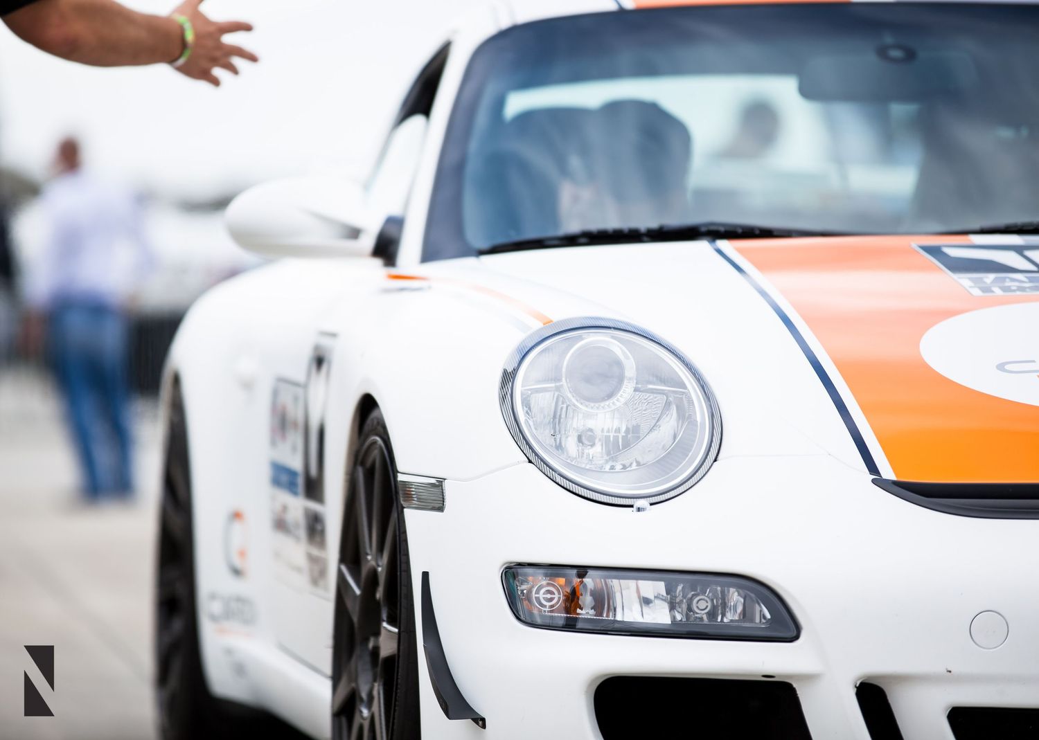 Closeup of a white Porsche 911 GT3 RS sports car with orange racing stripes showing headlight and front quarter panel detail.