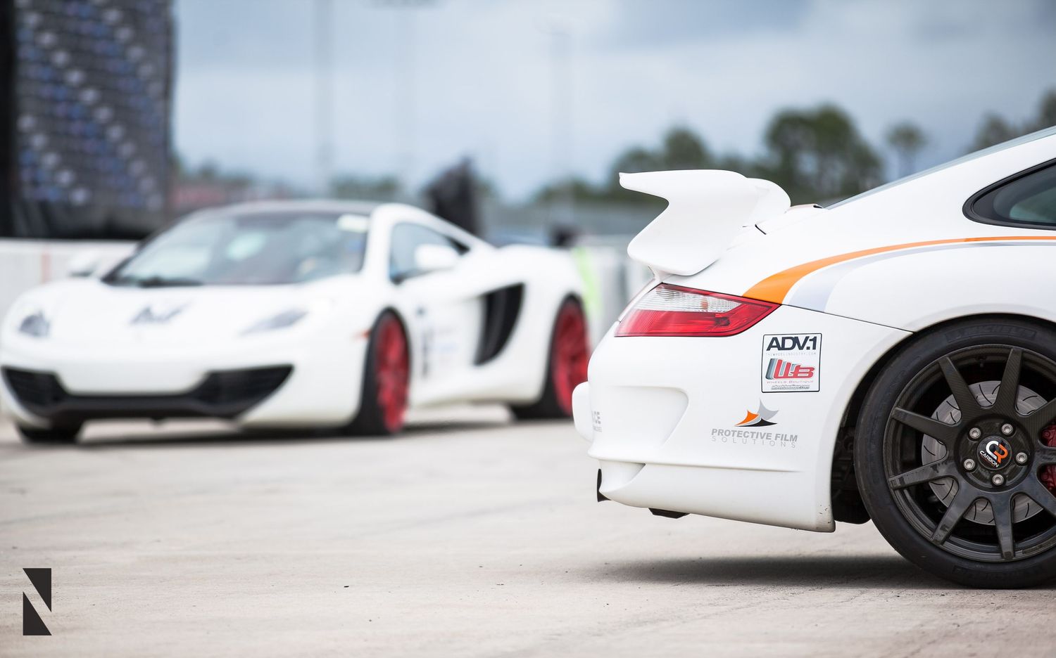 A white Porsche GT3 and McLaren MP4-12C supercar pair sit parked at a car event.
