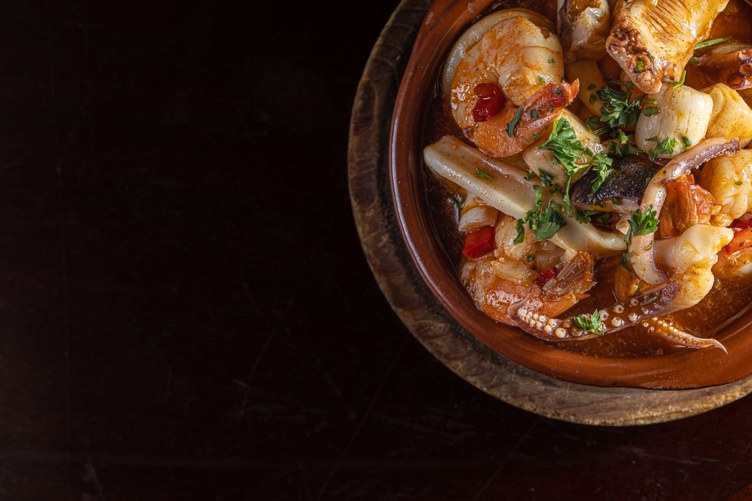 Seafood stew with shrimp and octopus in a rich tomato broth garnished with fresh herbs served in a rustic bowl.
