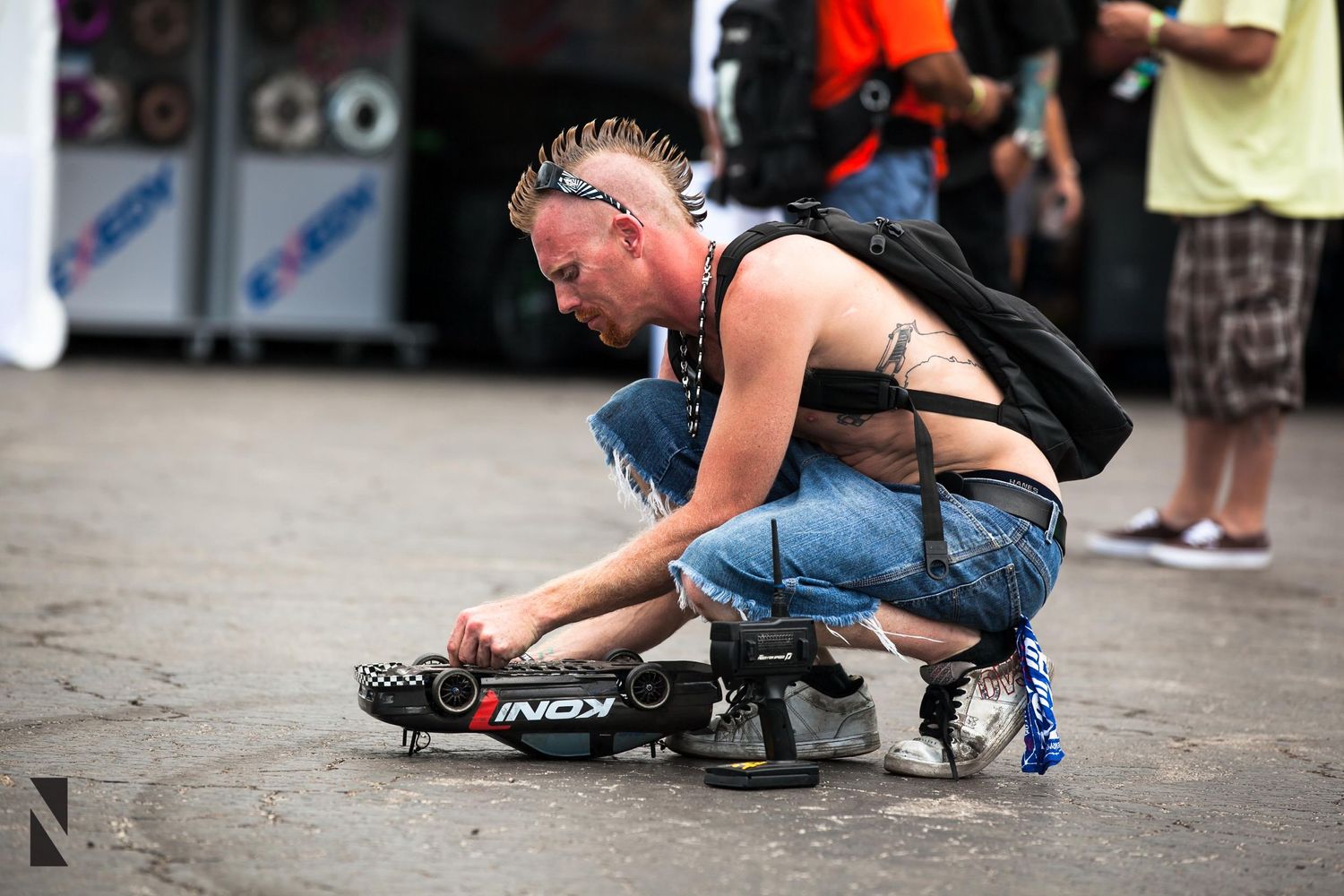 Person in jeans and tank top crouches down to adjust rollerblades or skates on urban pavement.