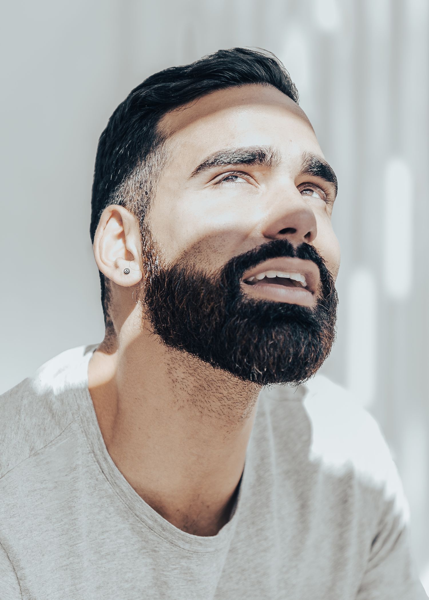 Close up portrait of smiling man with dark full beard wearing a light sweater and looking upward.