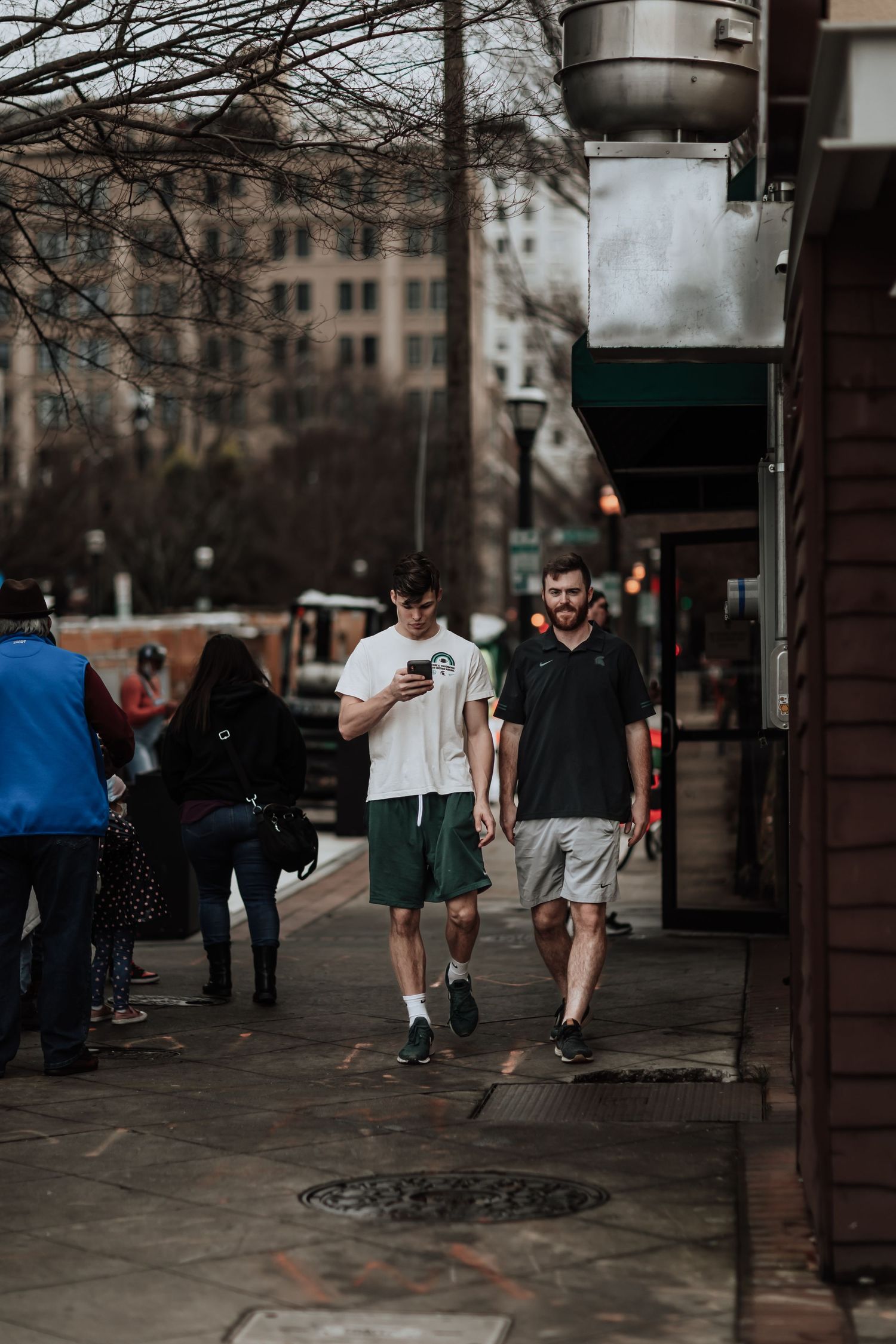 People walking on a crowded city sidewalk beneath tall buildings on an overcast day.