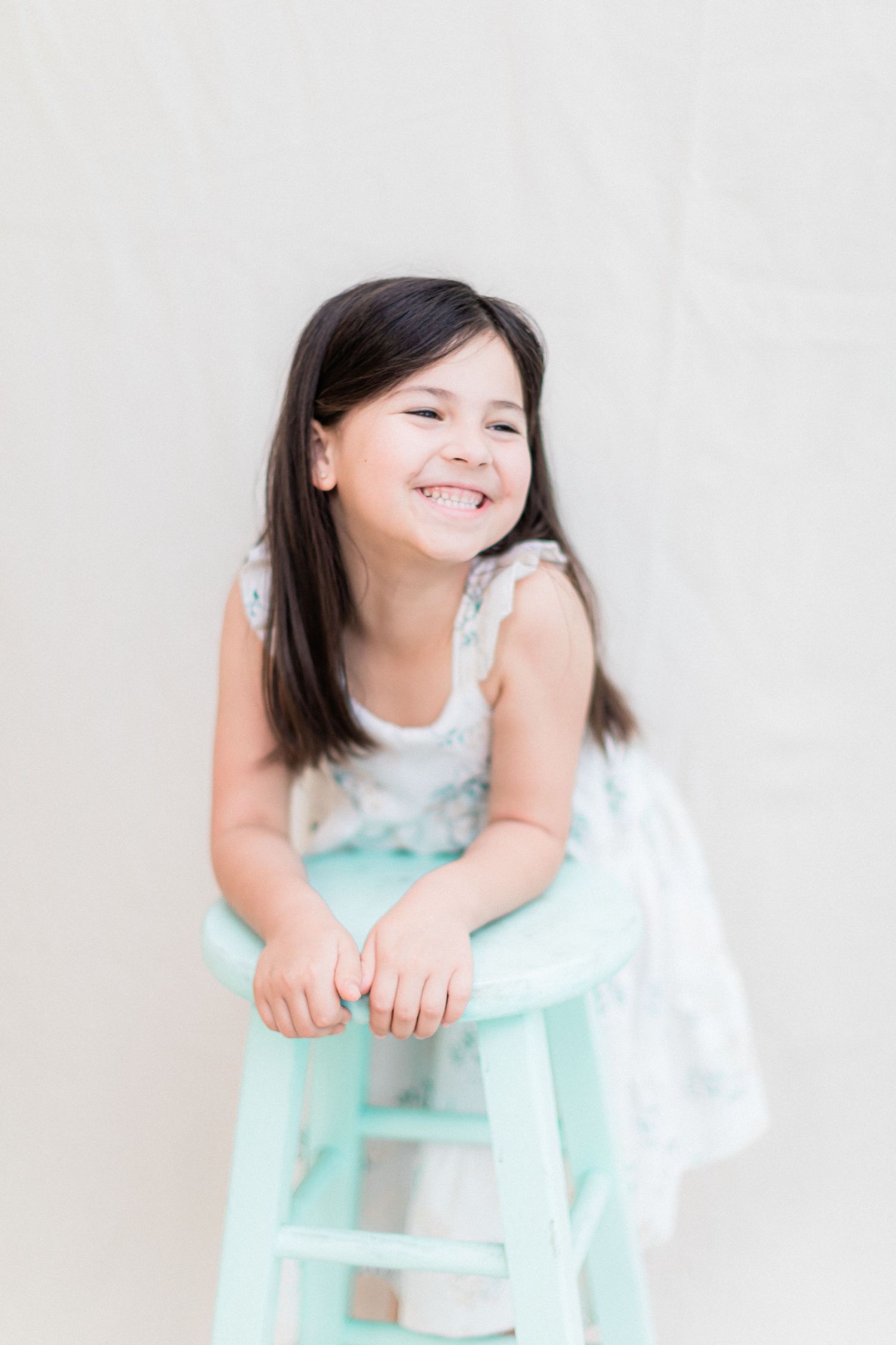 Joyful portrait on mint stool wearing white floral summer dress.