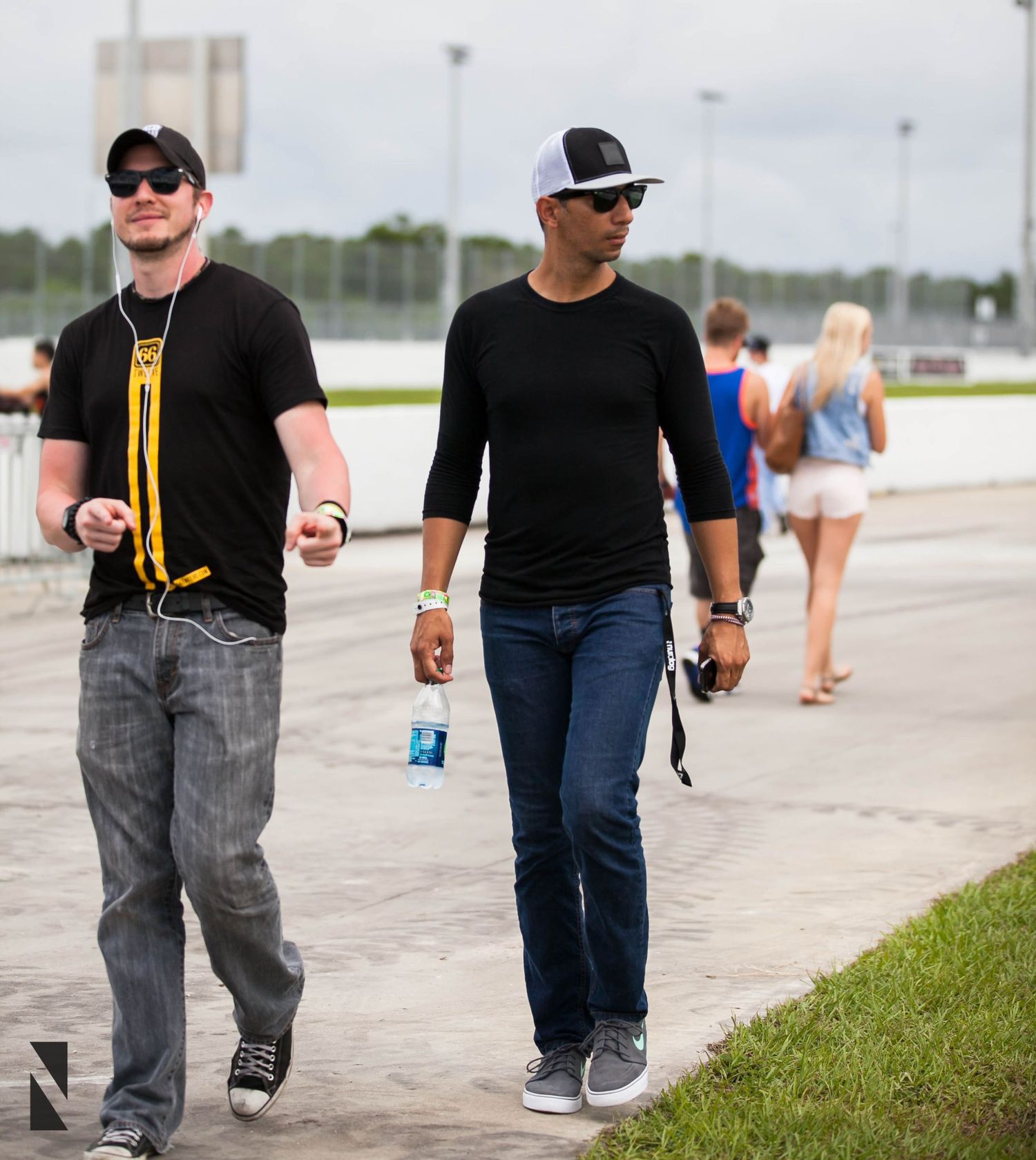Car enthusiasts walking on pavement at an outdoor automotive event.