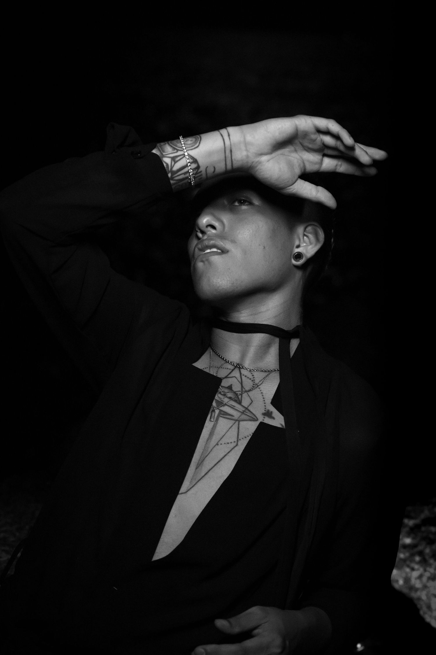 Artistic monochrome portrait showing tattooed arm and dramatic pose with hand covering face.
