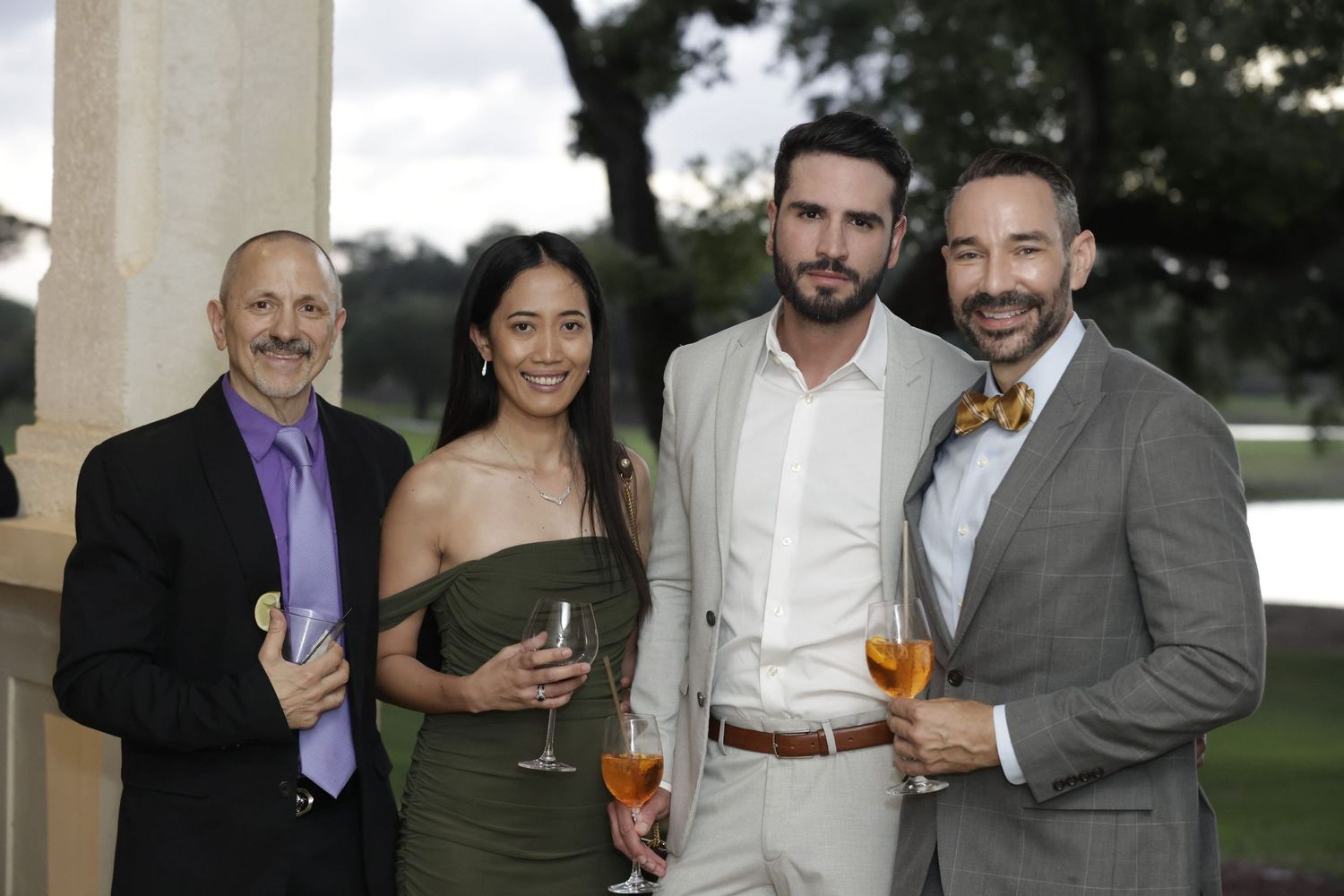A small group gathers outdoors holding cocktails and beverages at a social event.