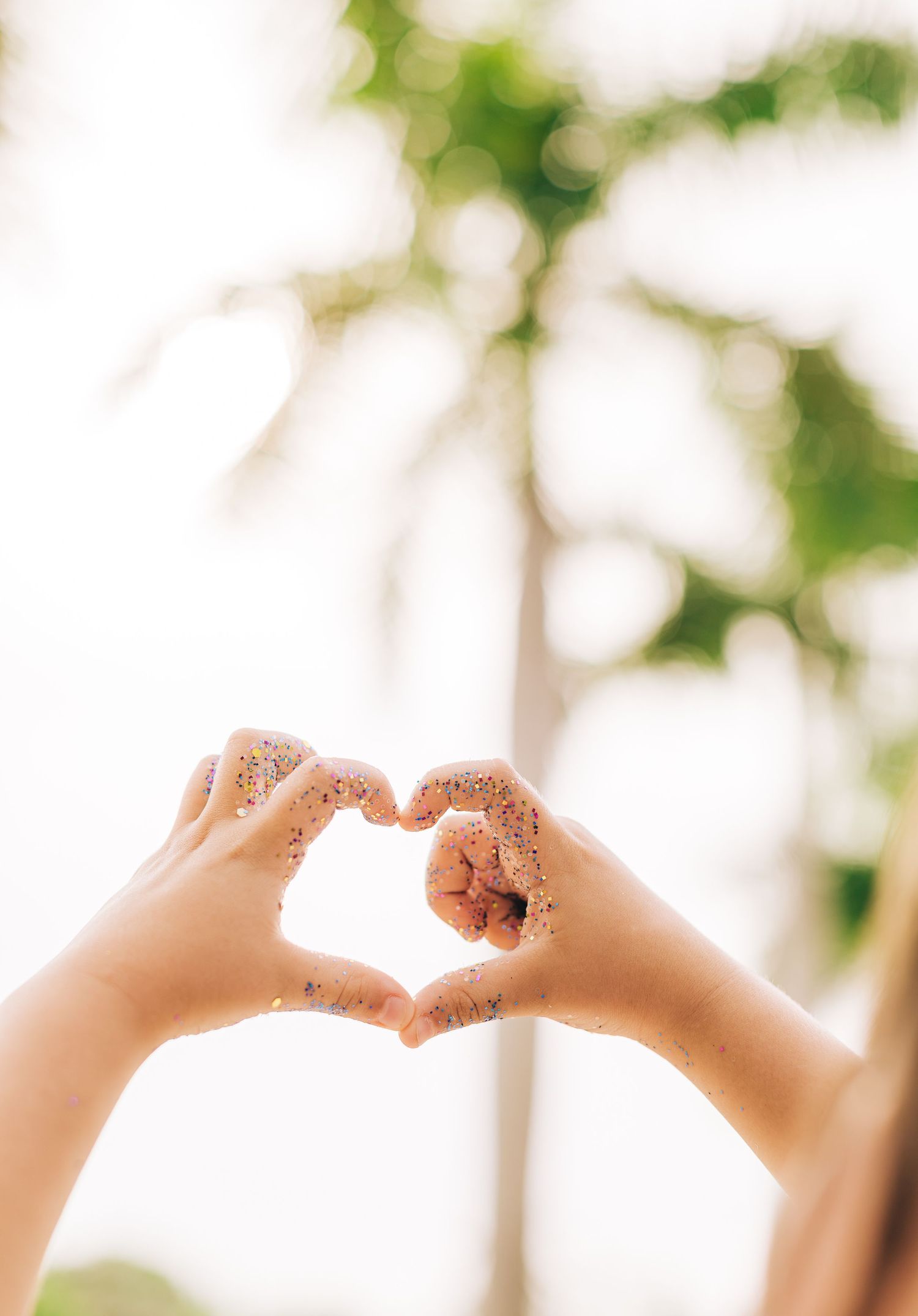 Hands forming a heart shape against a soft bokeh background with green foliage.