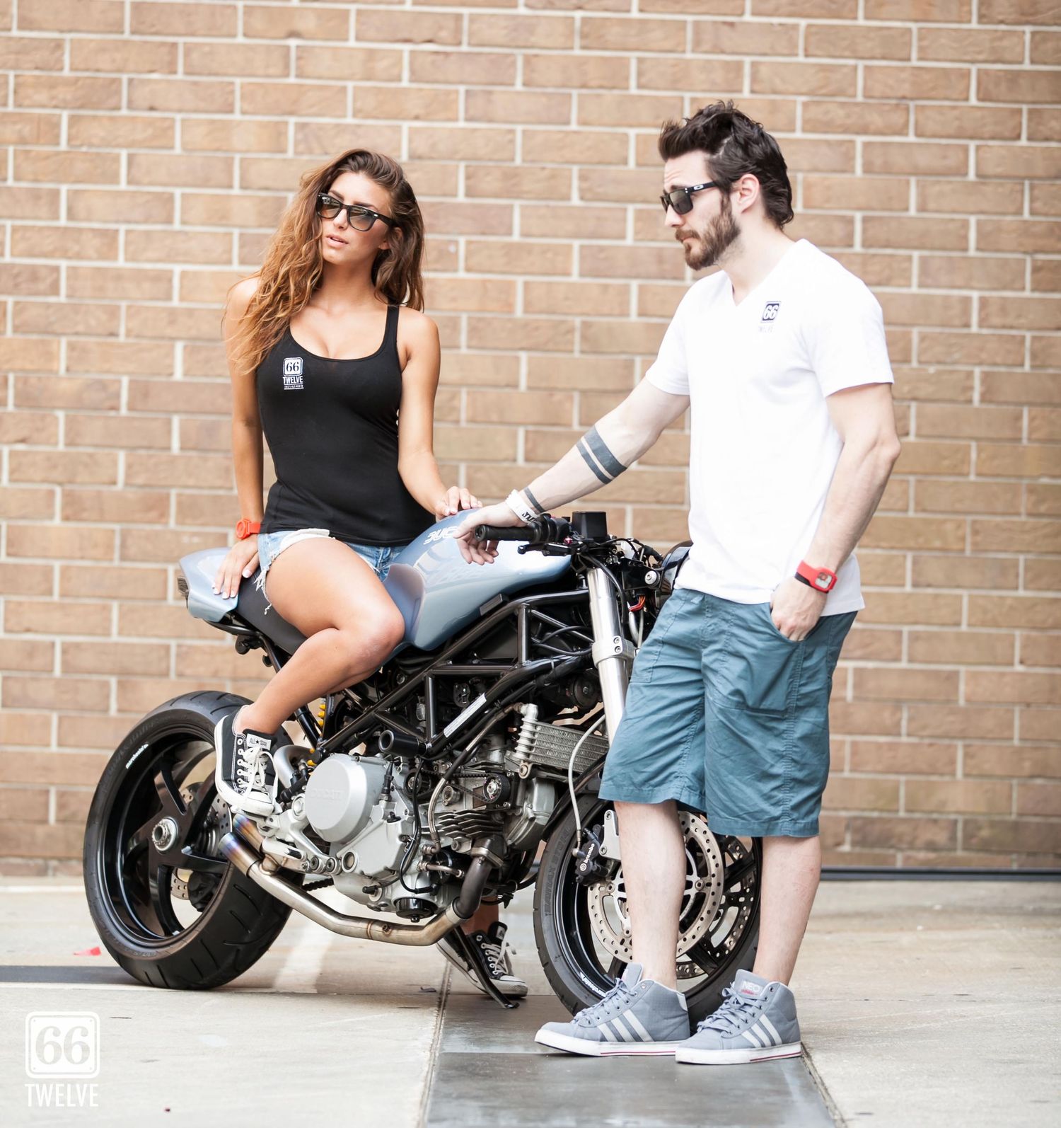 Ducati Monster motorcycle parked against brick wall with two people casually interacting beside it.