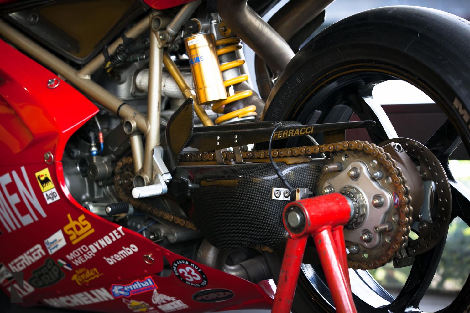 Close-up detail of a motorcycle's rear suspension showing gold shock absorber and chain drive mechanism.