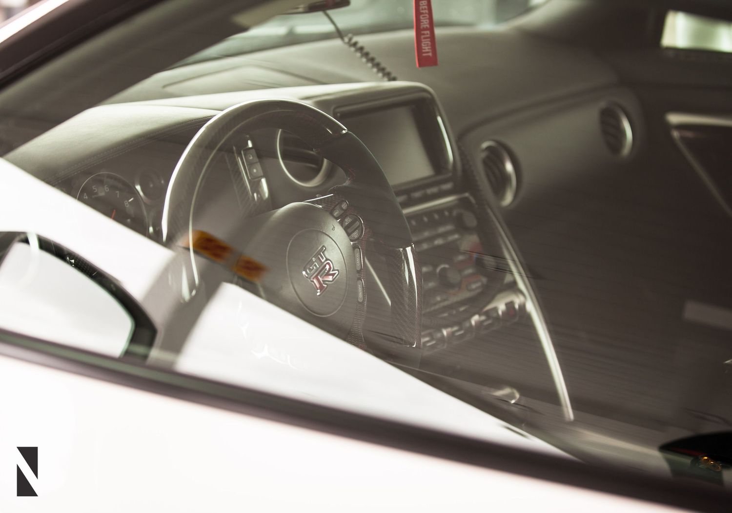 Interior view through car window showing modern dashboard with digital display and steering wheel in dark lighting.