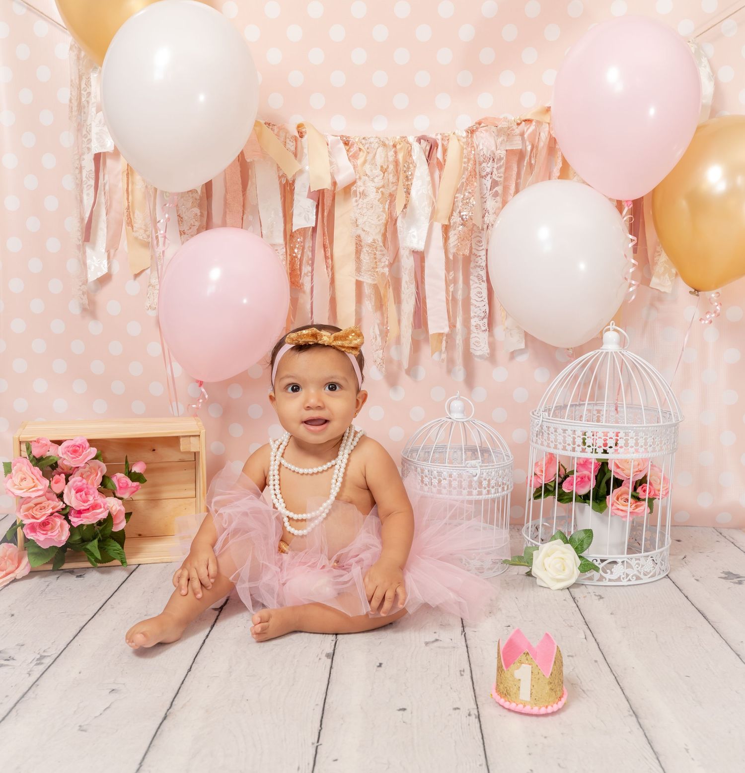 Decorative pink and white party setup with balloons, floral birdcages, and rose bouquets on rustic white wooden floor.