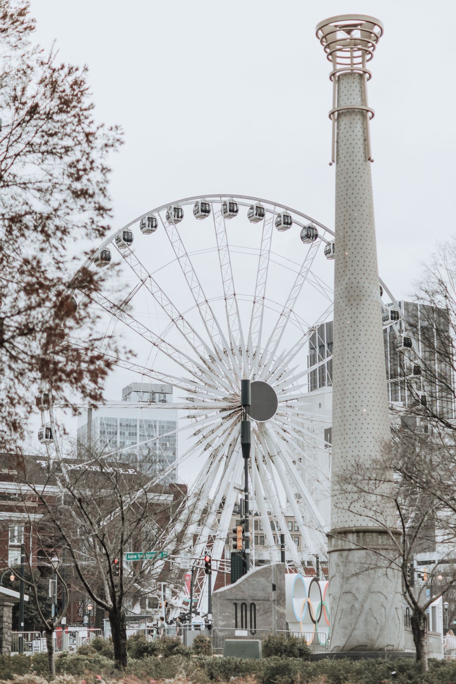 Large ferris wheel and monument tower in urban park during winter.