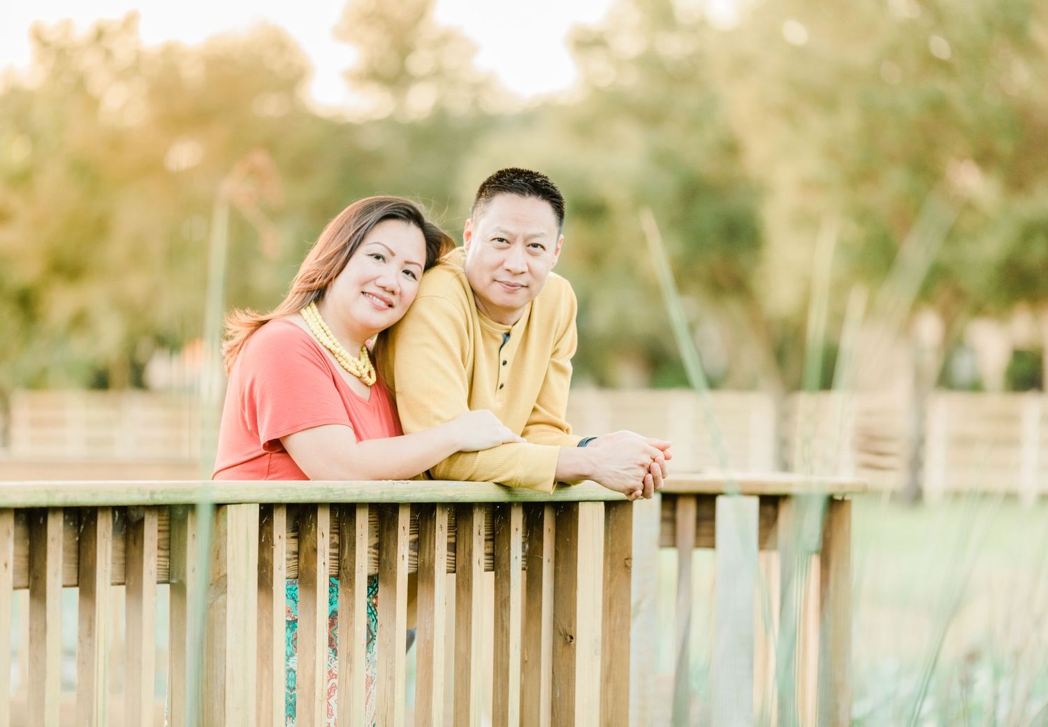 A couple leans on a wooden railing together in warm evening light.
