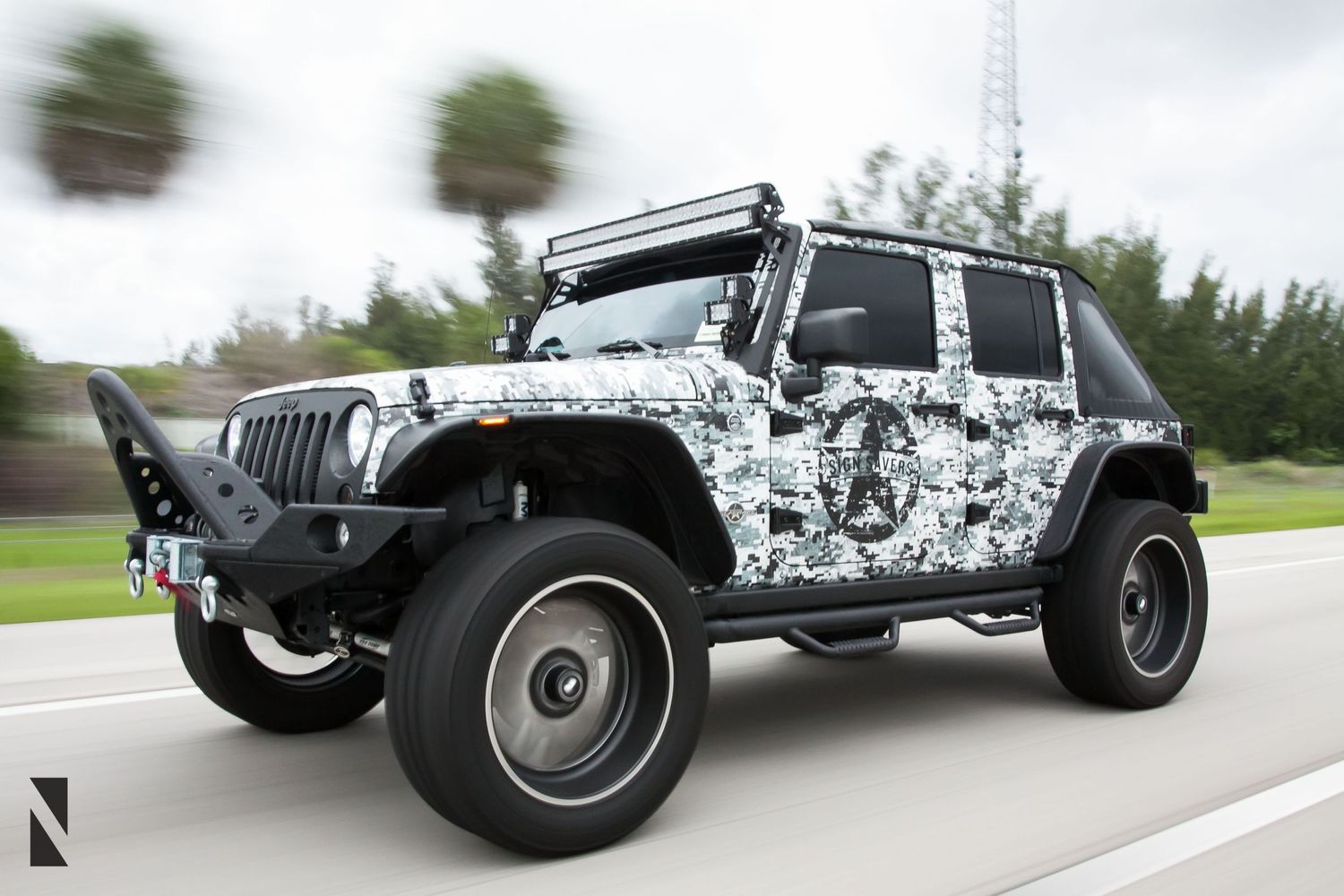 Custom Jeep Wrangler with digital camo wrap and lifted suspension driving on the road.