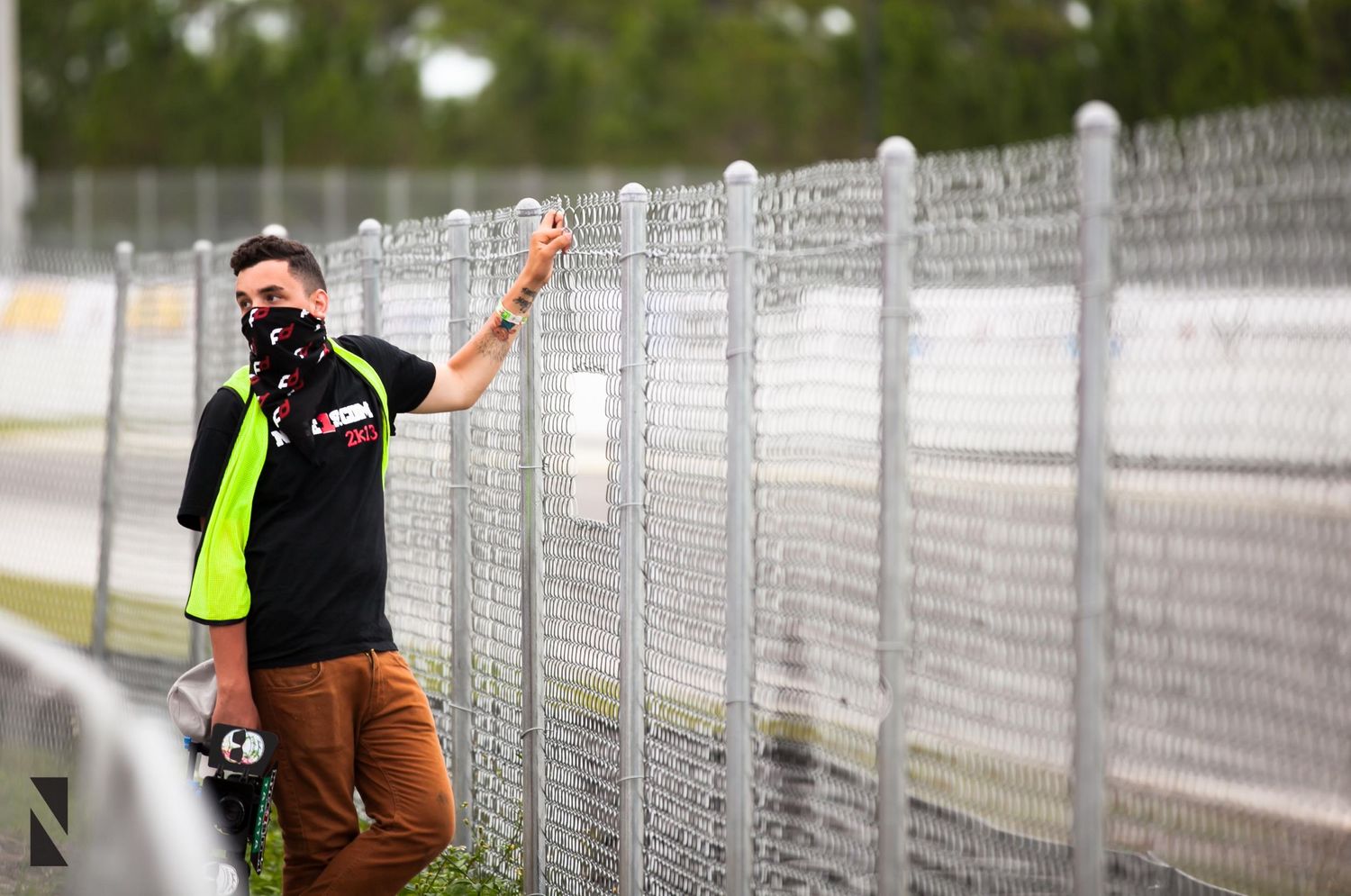 Racing enthusiast gestures while standing by safety fence at motorsport track.