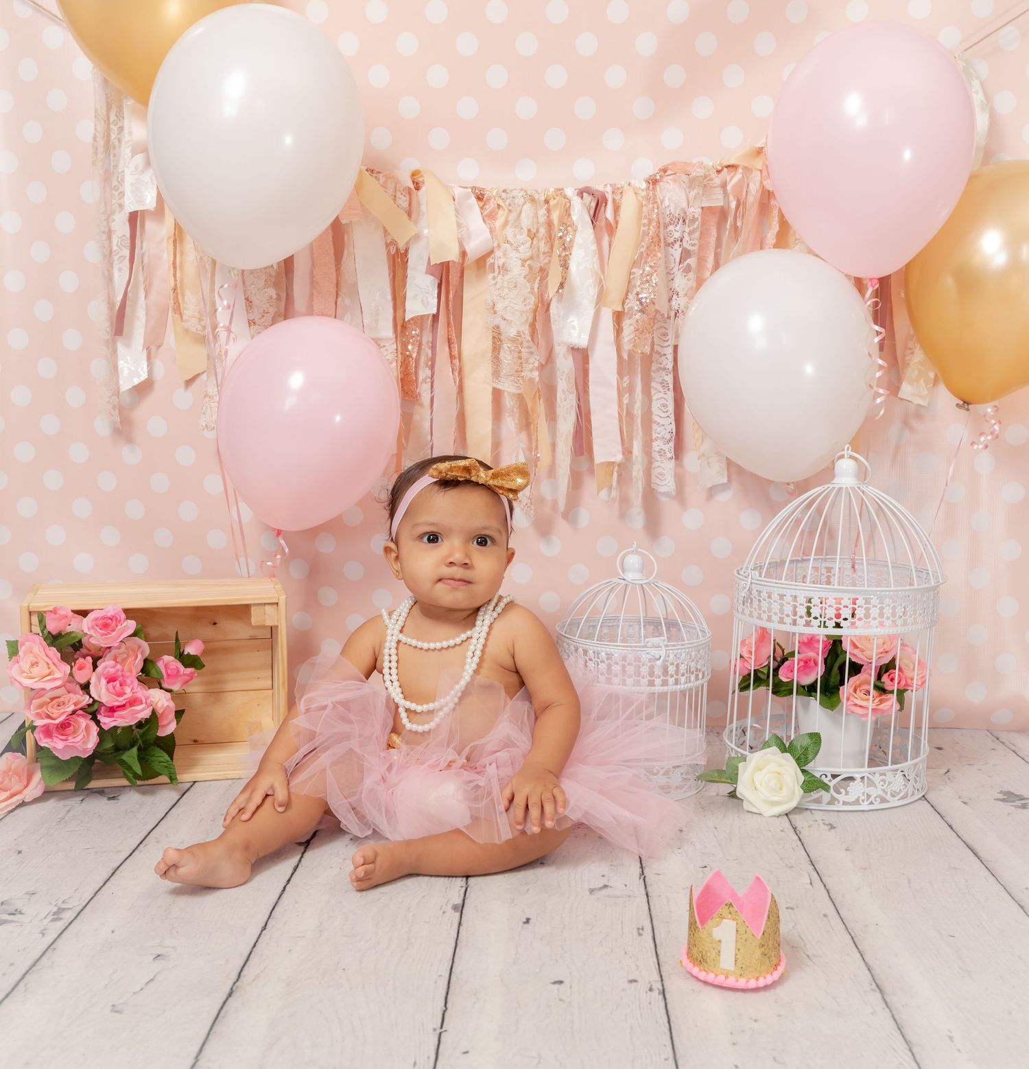 Pretty pink and gold balloon party setup with flowers, tulle fabric, vintage birdcages and white wood floors.