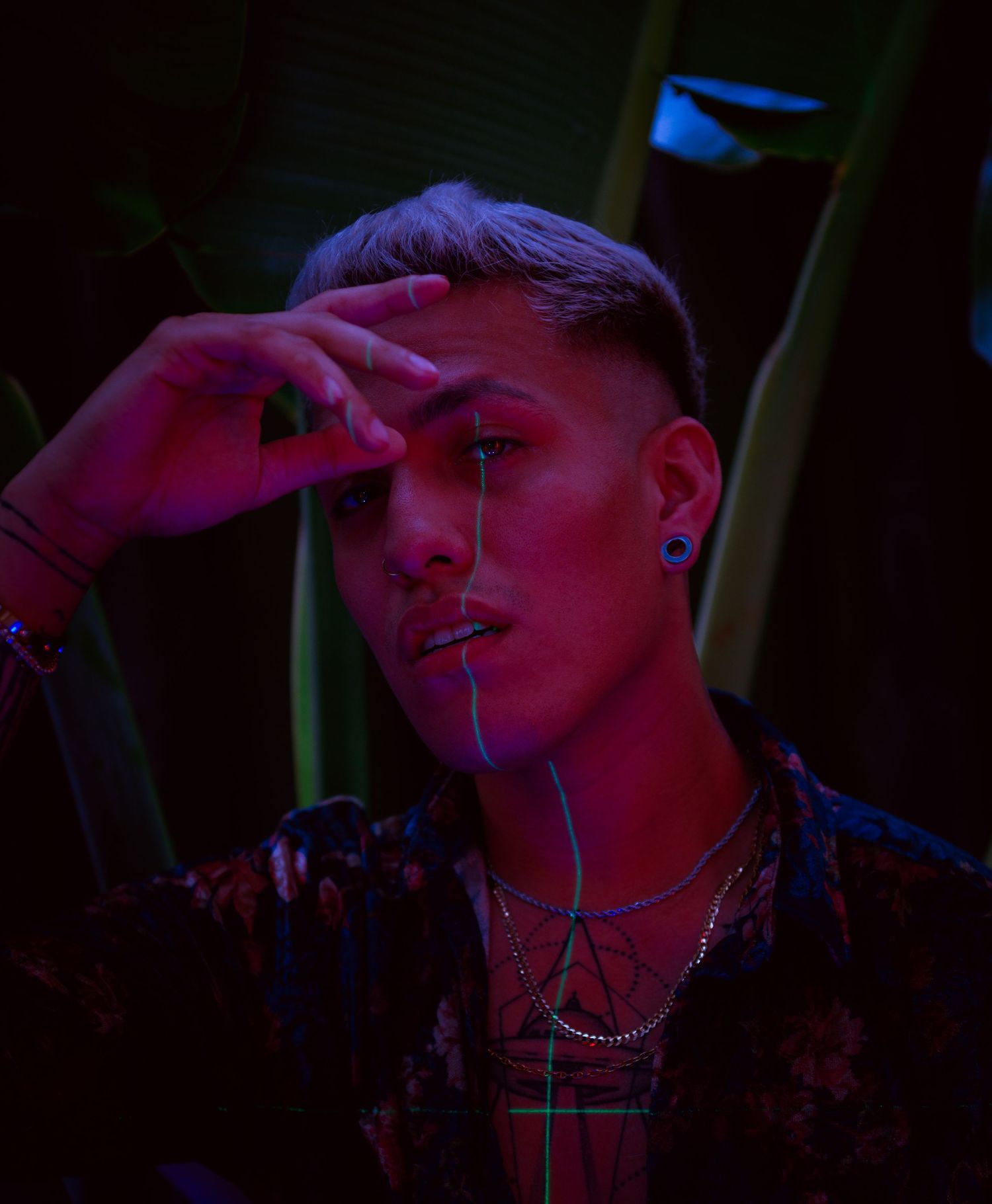 Moody portrait with neon lighting and jewelry against dark background.
