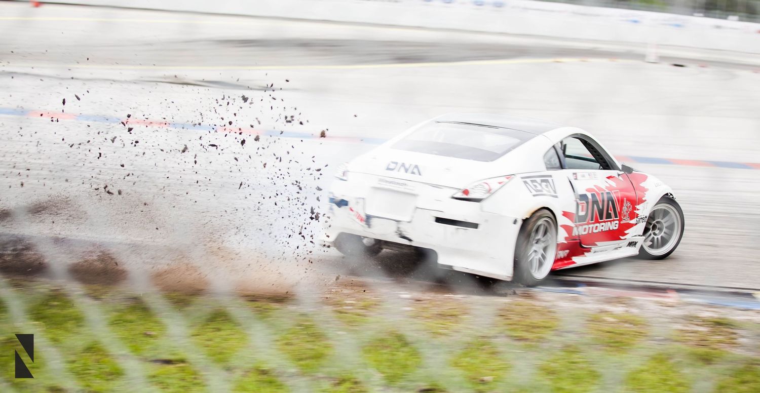 White sports car drifting on wet track with water spray flying behind it.