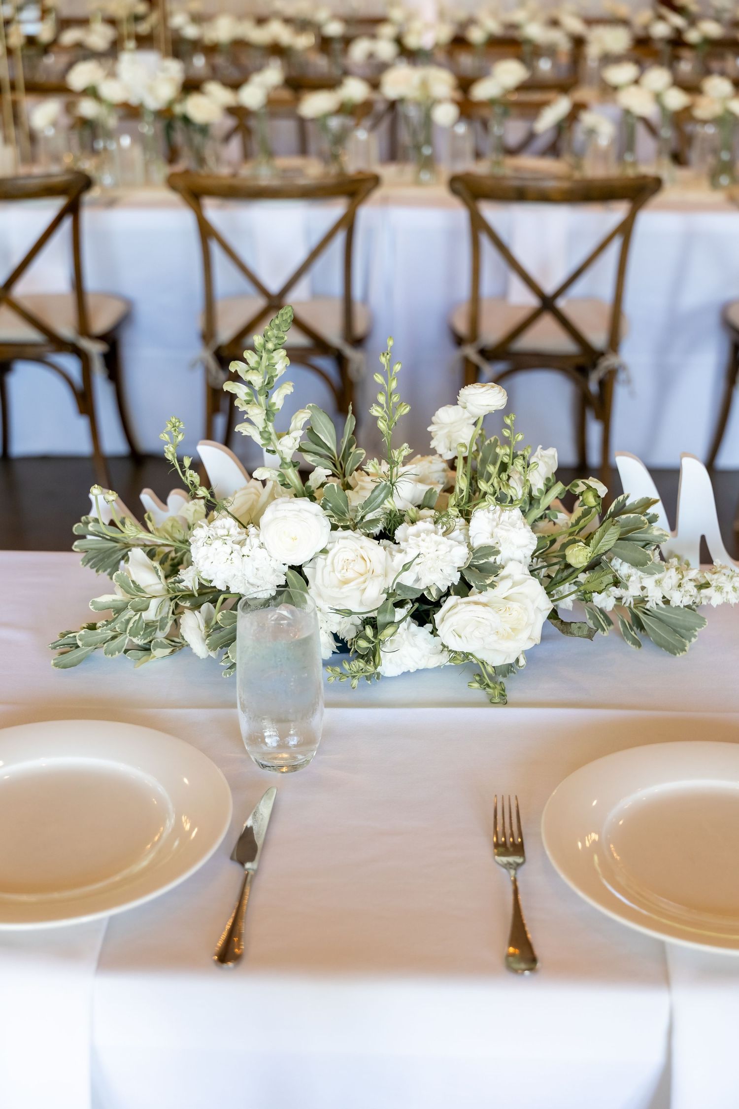 Elegant wedding table setting with white floral centerpieces and cross-back chairs.