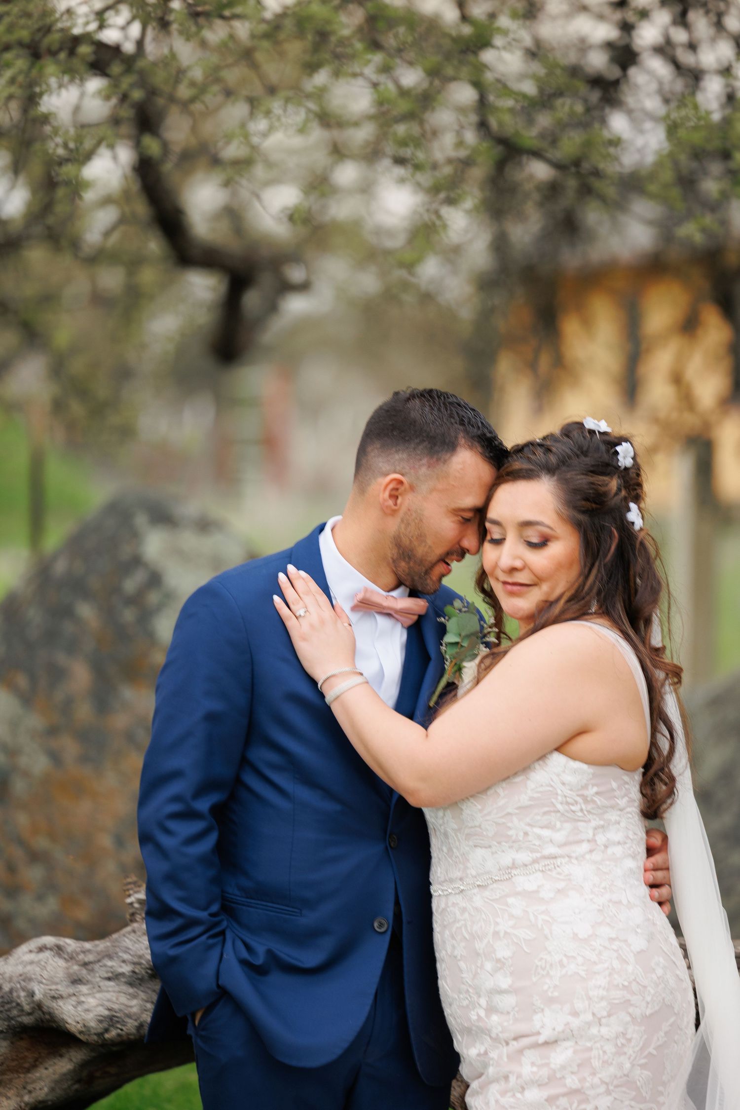Romantic wedding couple embraces outdoors under blooming spring trees in natural light.