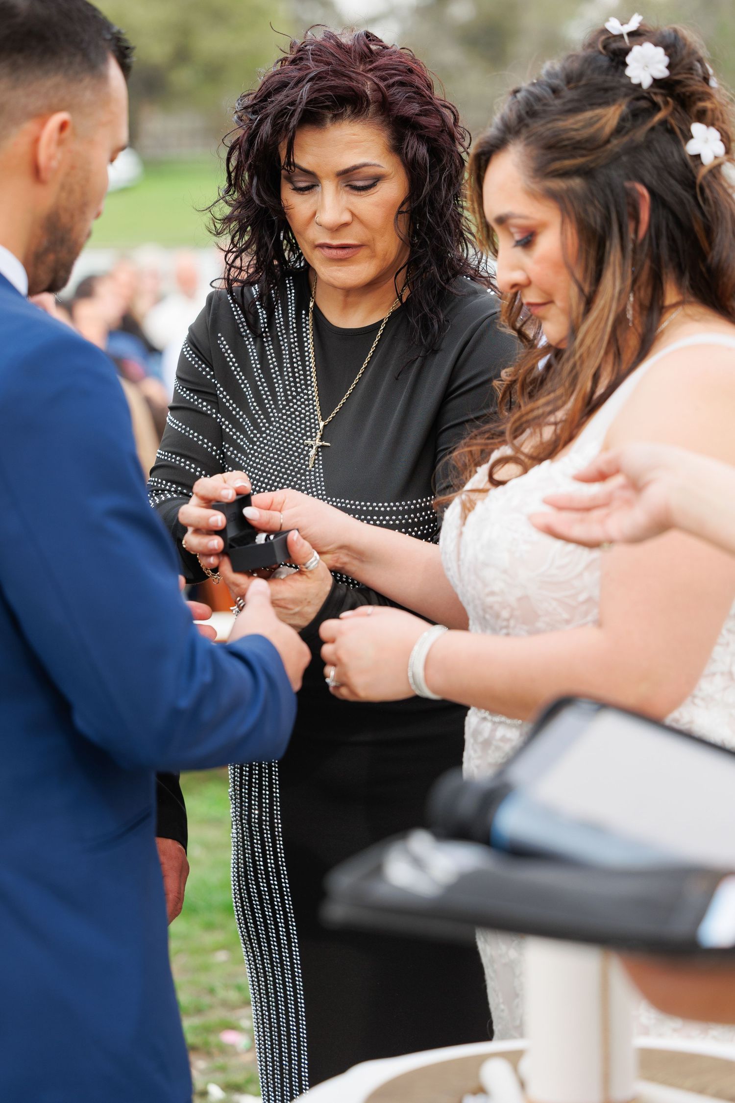 A group gathers closely together looking down at something during an outdoor wedding ceremony.