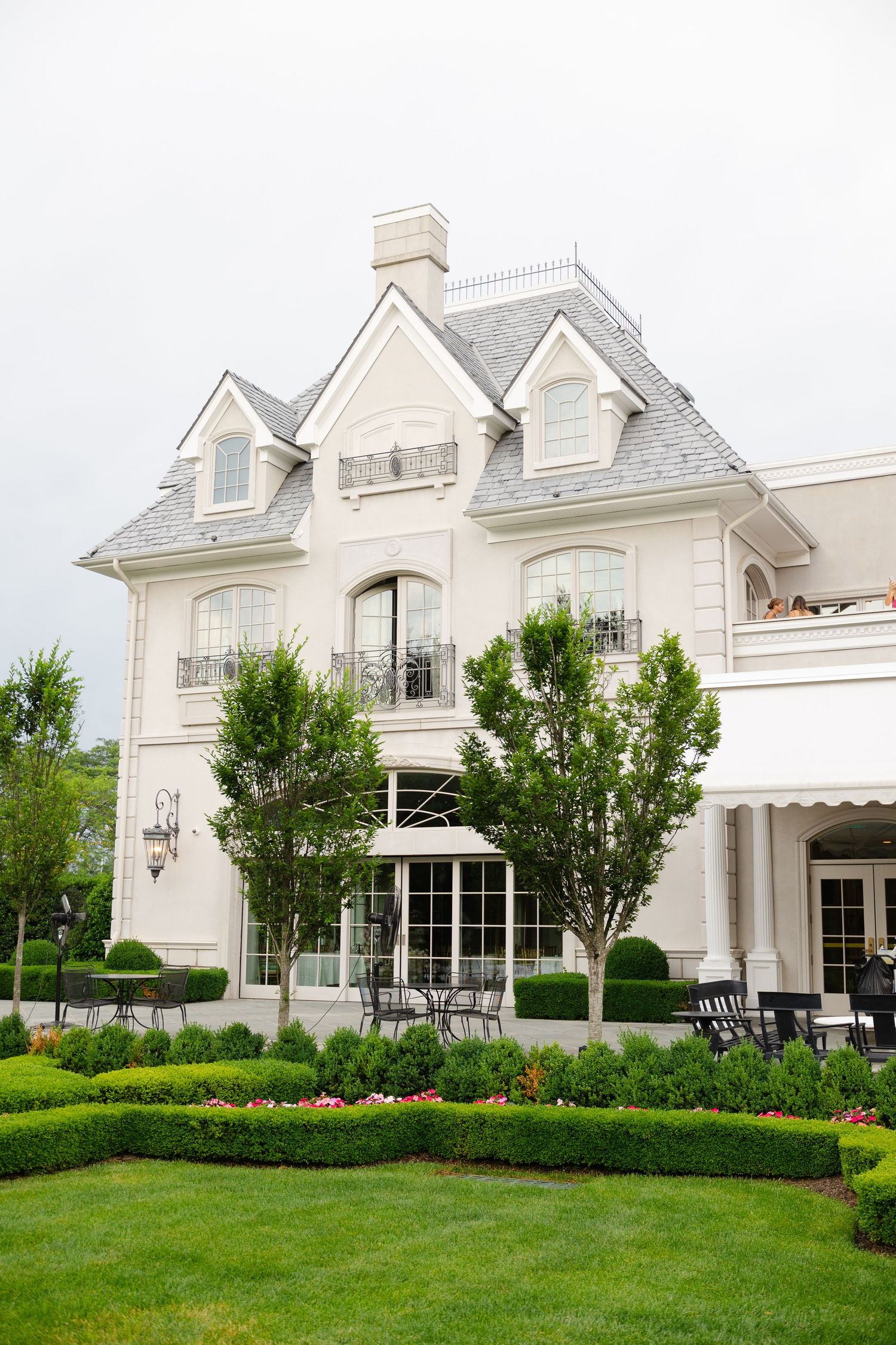 Elegant white mansion with dormer windows and manicured landscaping shown from multiple angles on a lush green lawn.