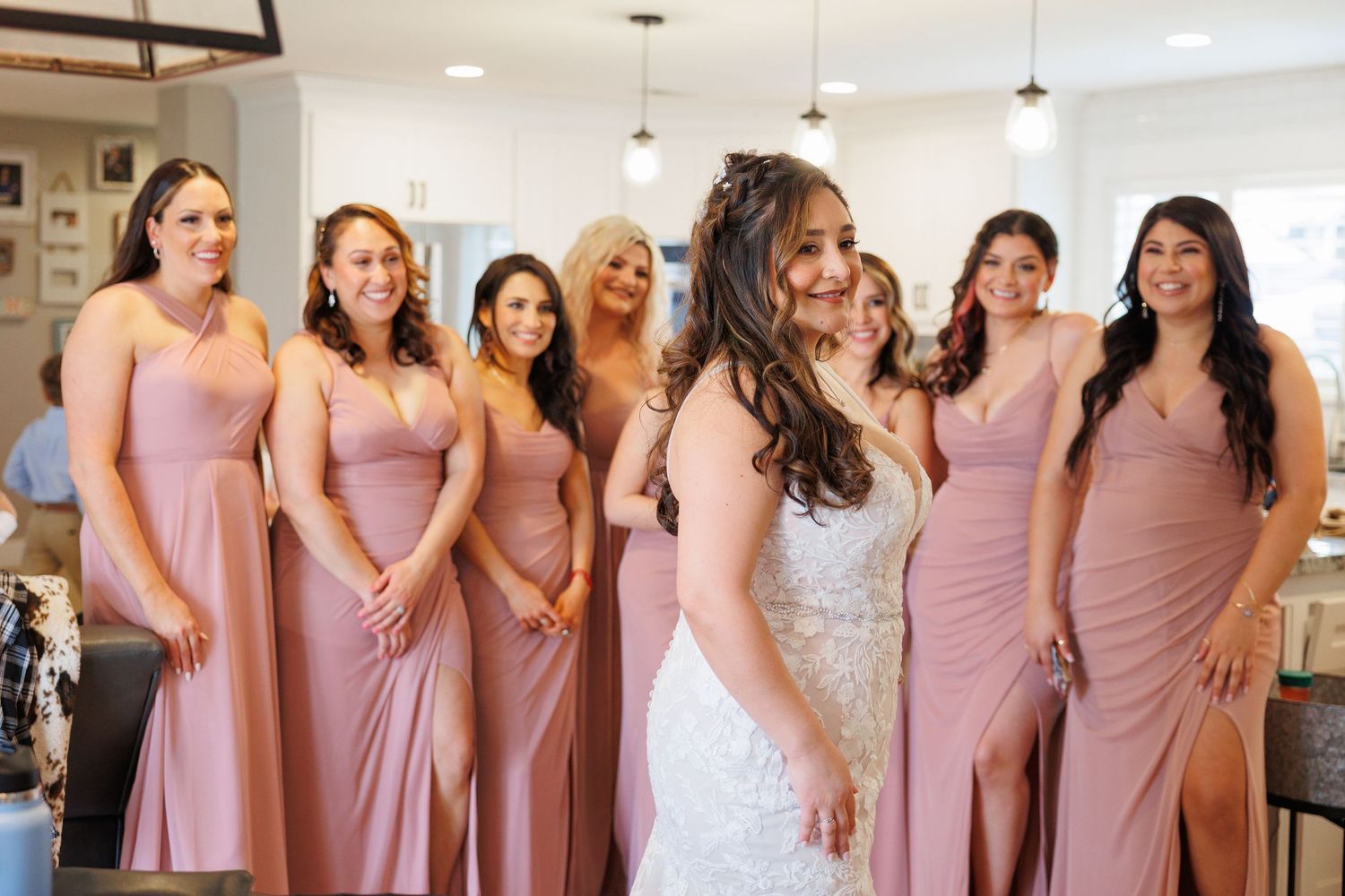 Bridesmaids wearing dusty rose pink dresses pose together in a bright indoor venue during a wedding celebration.