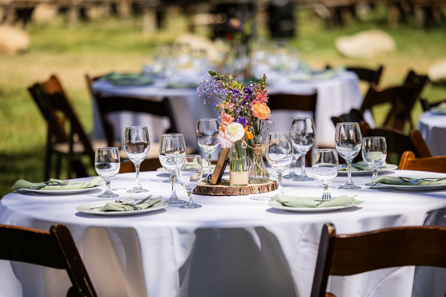 Elegant outdoor wedding reception tables decorated with white linens, glassware, and floral centerpieces at sunset.
