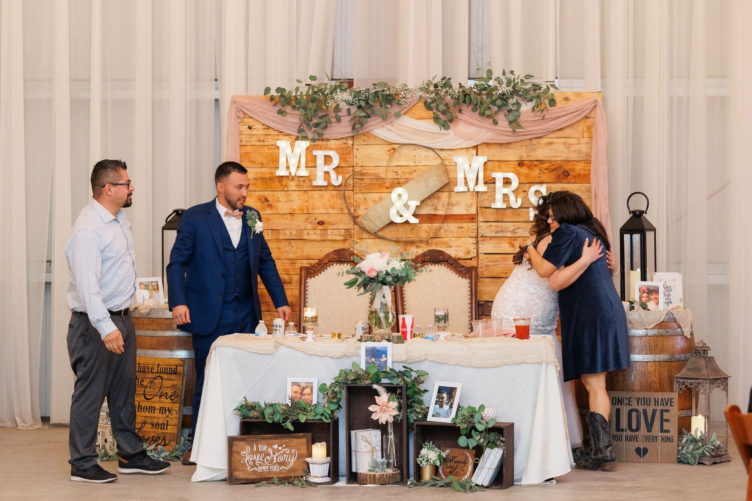 Wedding reception decor features rustic wood walls with Mr and Mrs signs, white floral arrangements, and elegant table settings.