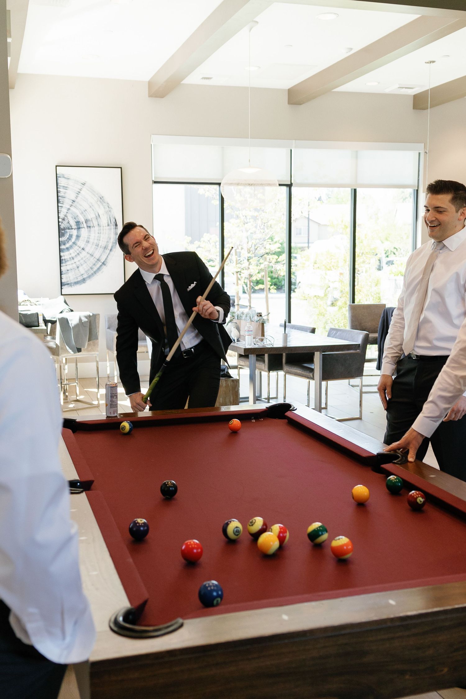 Friends enjoying a game of pool at an upscale venue with bright windows and modern decor.