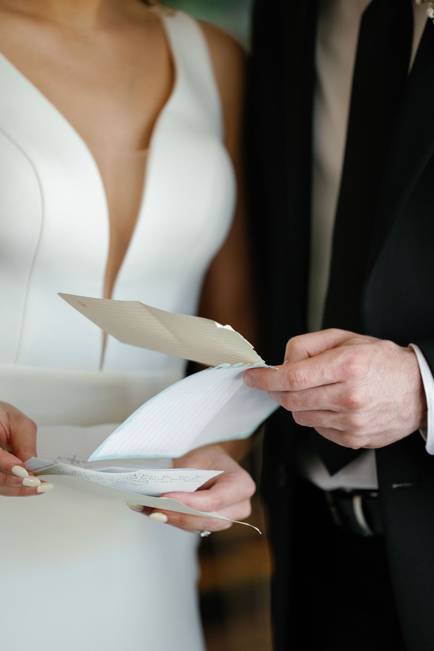 Close-up of a bride in white dress and groom exchanging handwritten notes or letters during an intimate wedding moment.