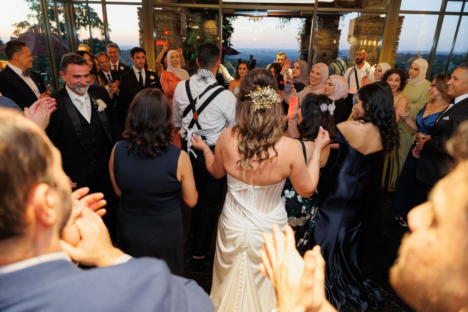 Wedding guests dance and celebrate together on a crowded dance floor at an indoor reception venue.