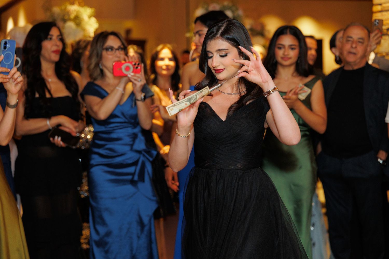 Wedding guests dance and celebrate together on a dimly lit dance floor at an evening reception.