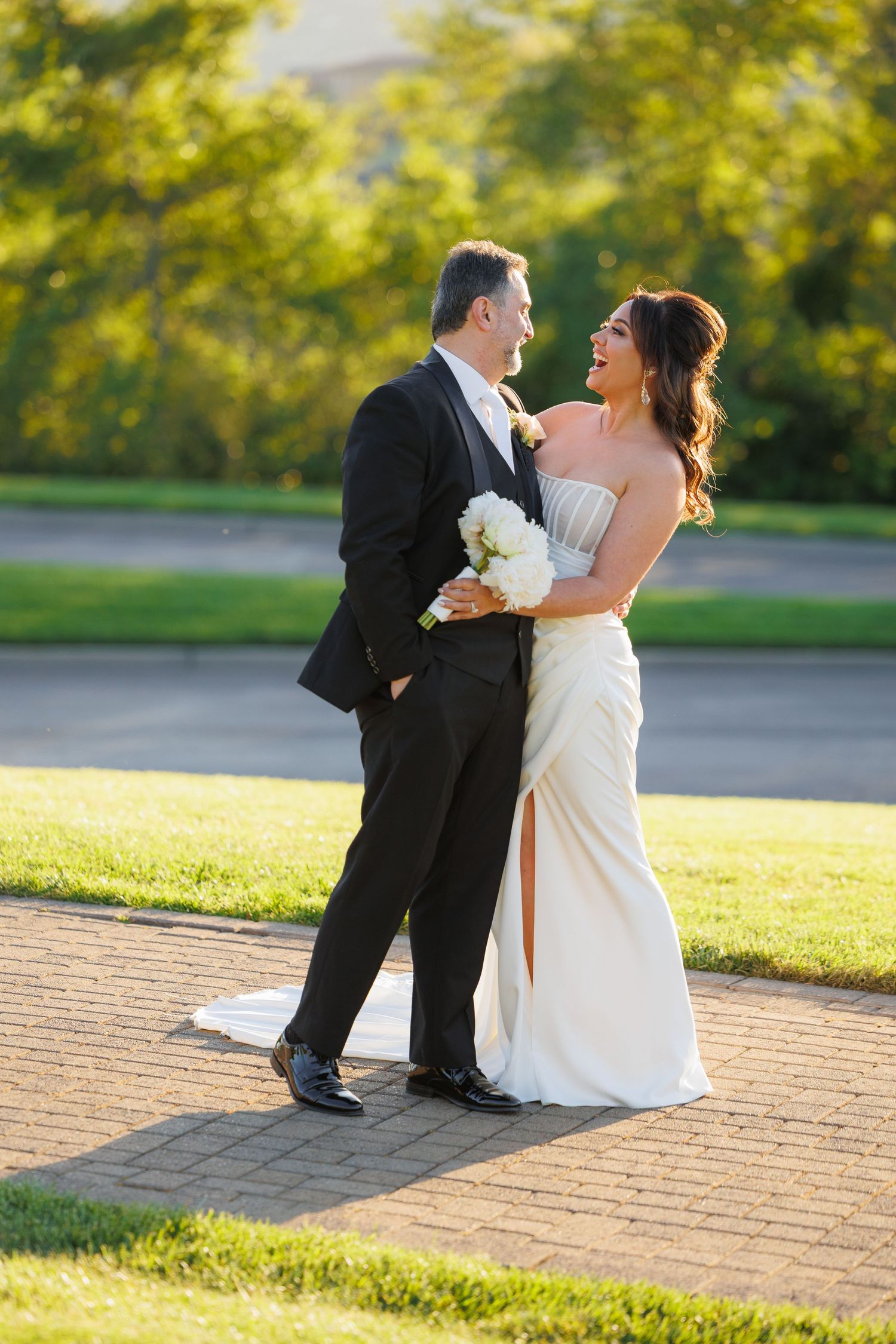 Couple in wedding attire sharing a romantic moment on brick pavement at sunset in a park setting.